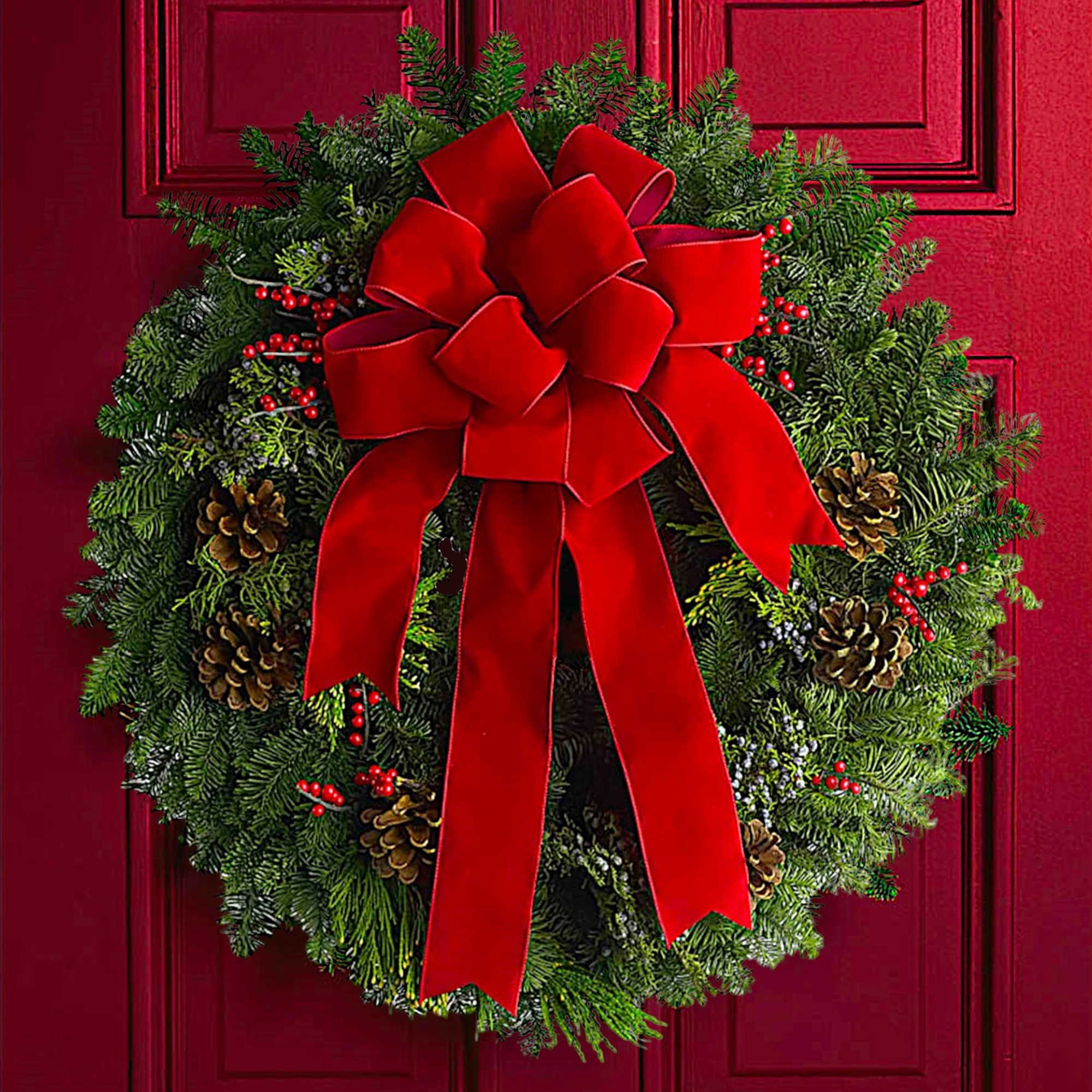 Christmas wreath with a red bow, pinecones, and berries on a red door