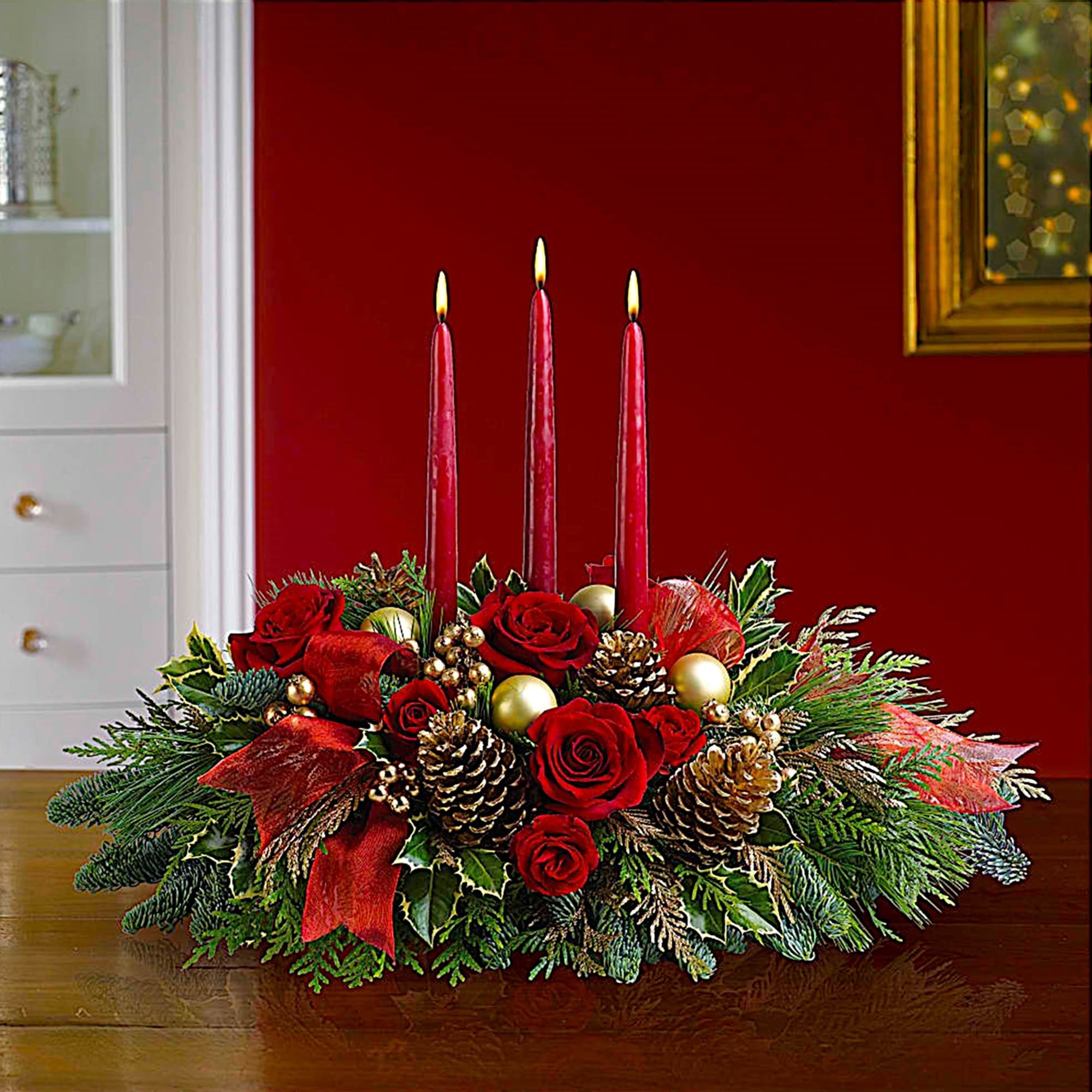 Red rose centerpiece with three lit taper candles and pinecones