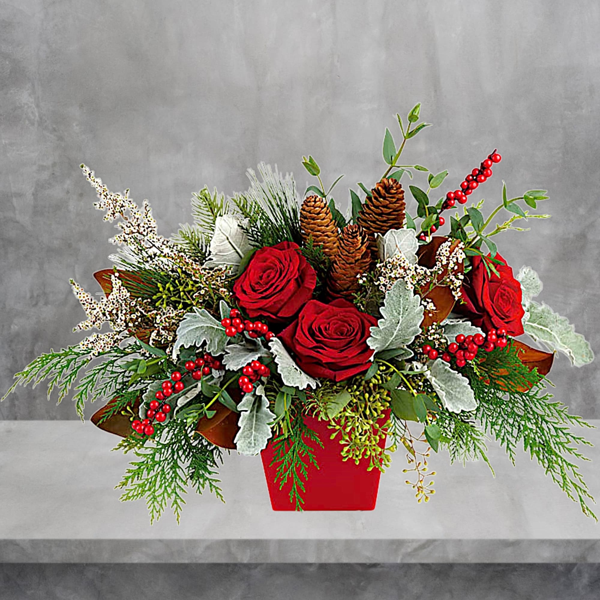 Red roses in a red vase with pinecones and winter greenery
