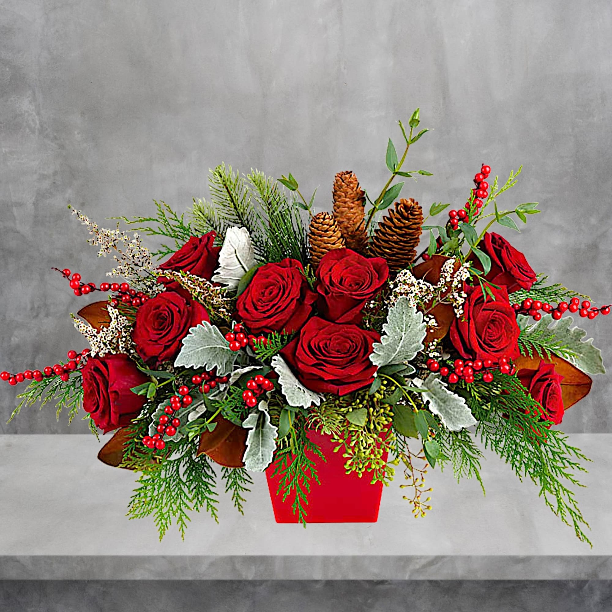 Red roses in a red container with pinecones and berries