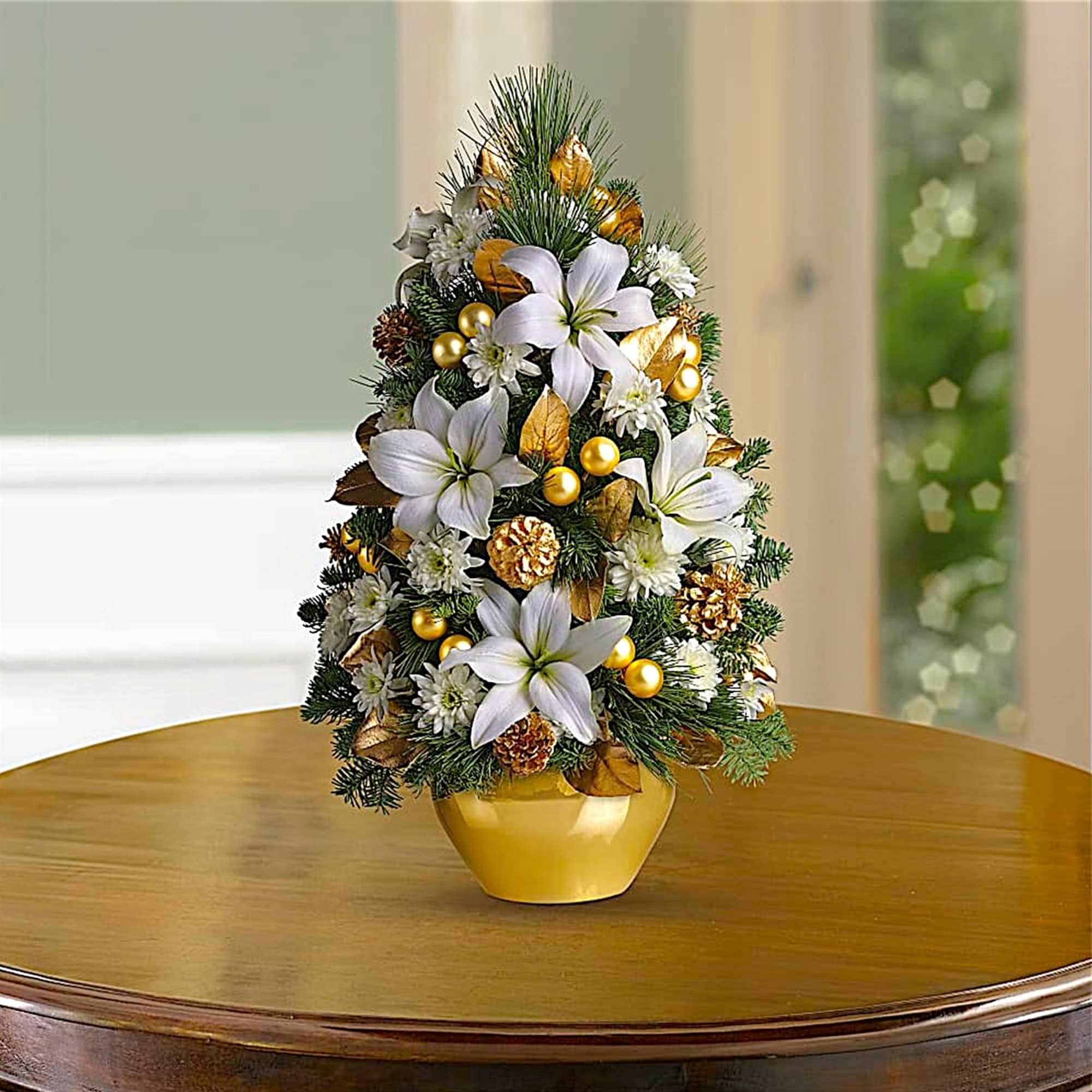 Christmas tree arrangement with white flowers and gold ornaments in a gold pot