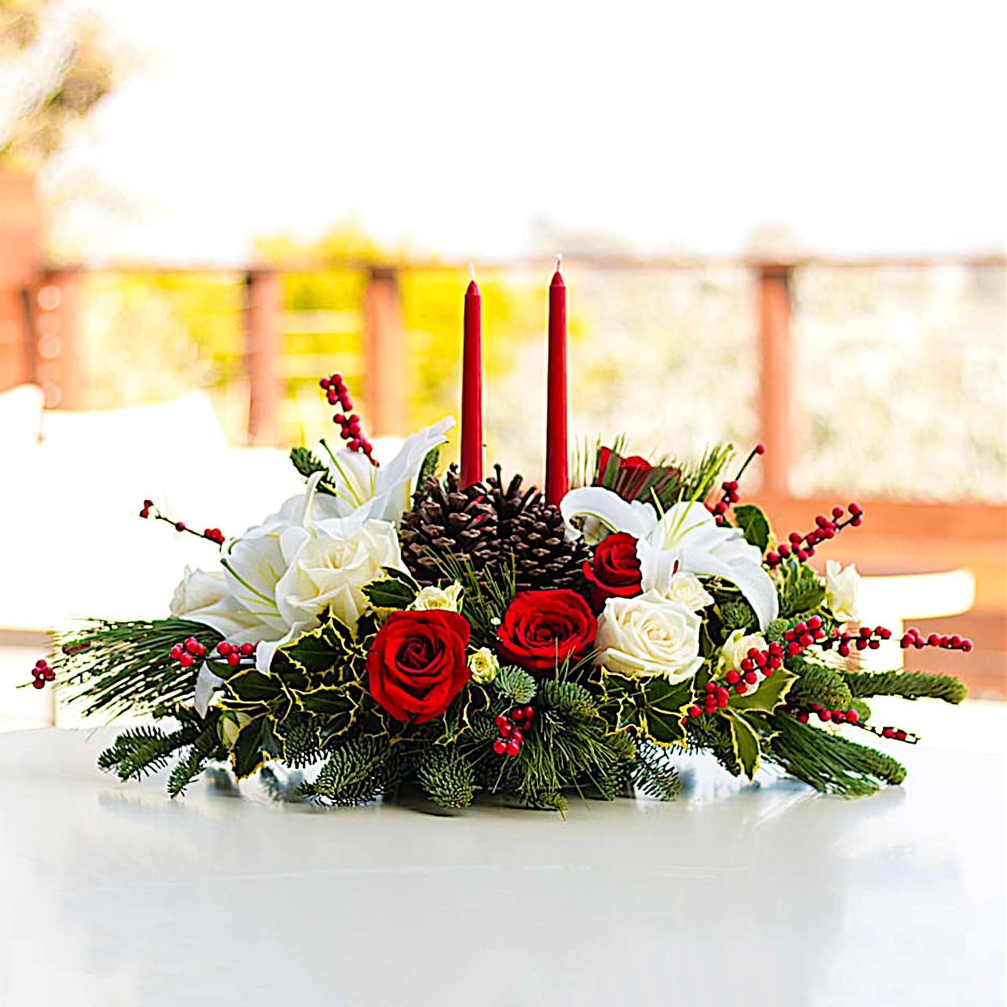 Holiday centerpiece with red candles, roses, lilies, and pinecones