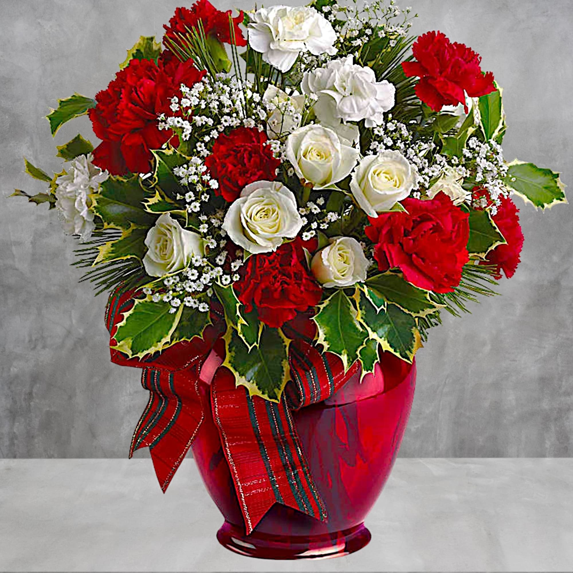 Red and white rose and carnation arrangement in a red vase with ribbon
