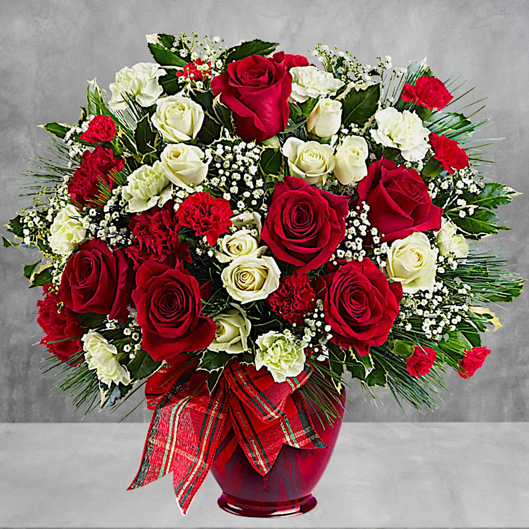 Red and white rose arrangement in a red vase with a plaid ribbon
