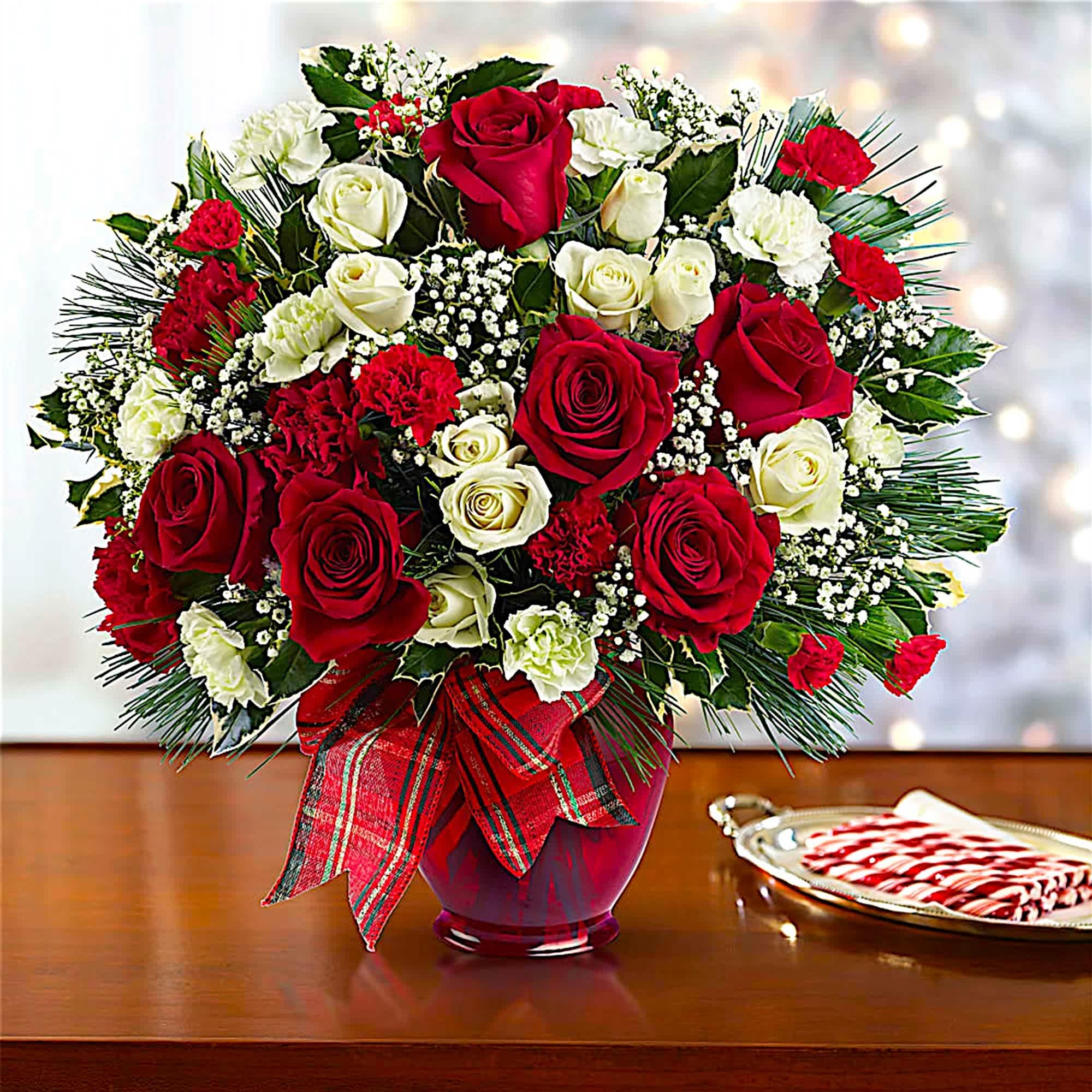 Bouquet of red and white roses in a red vase with a plaid ribbon
