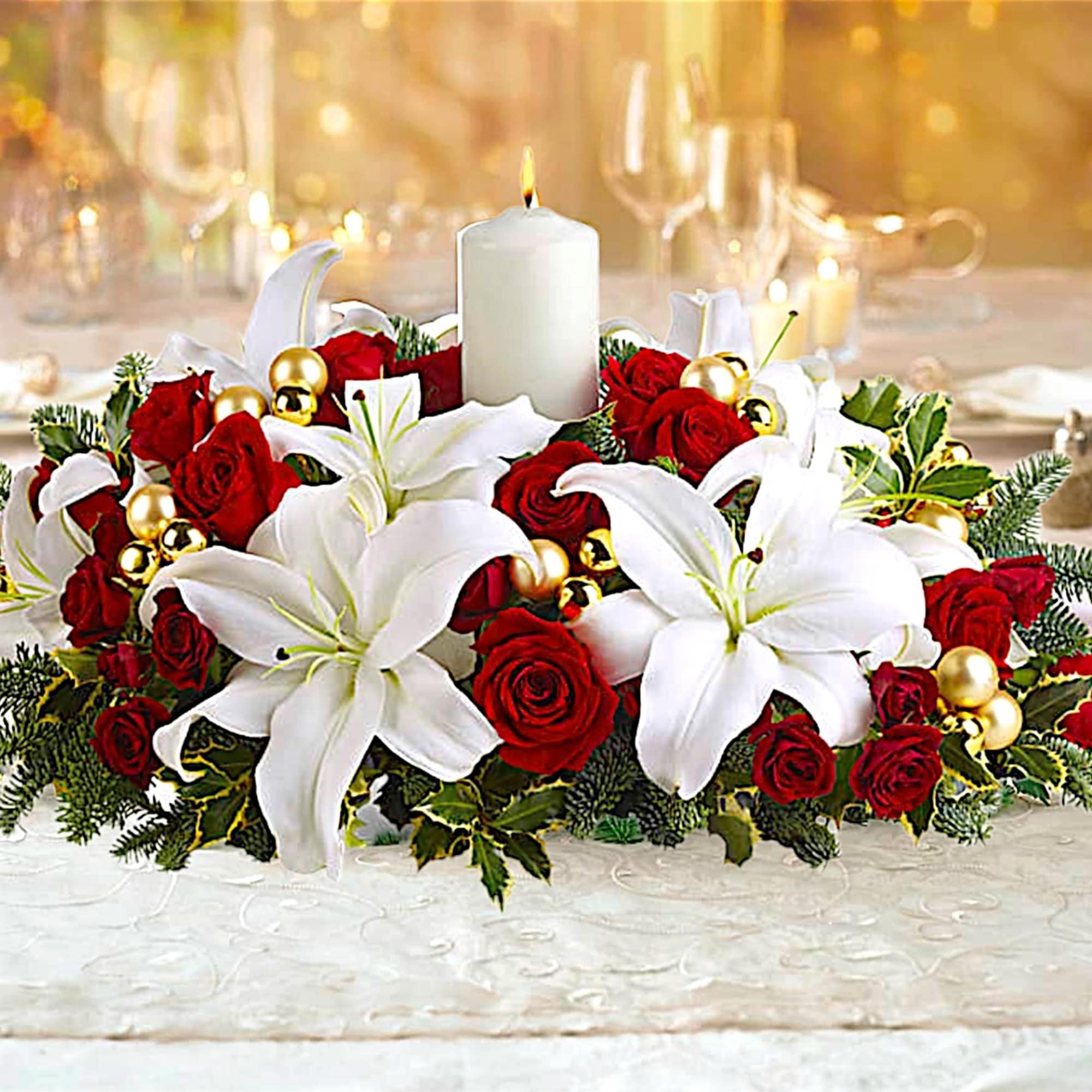 Red roses and white lilies arranged around a white candle on a table.
