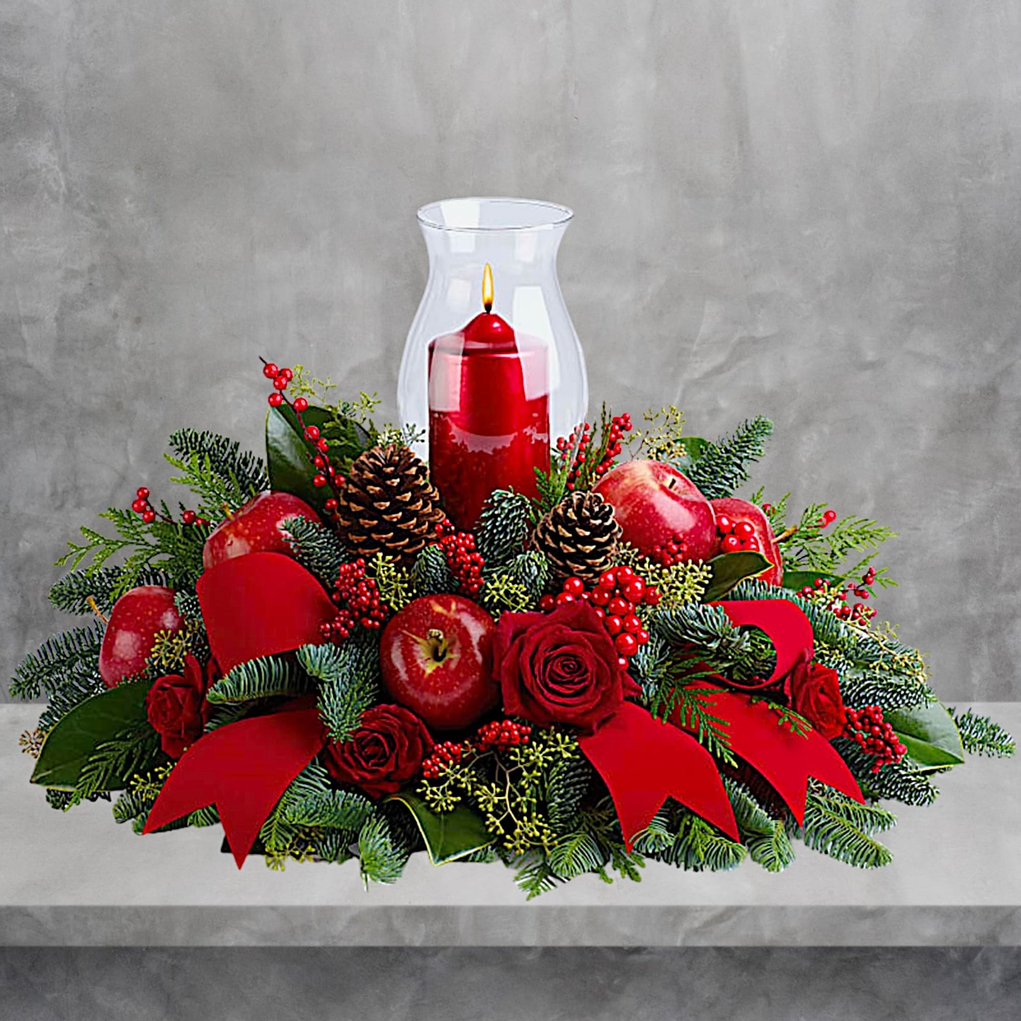 Holiday centerpiece with a red candle in a glass hurricane and apples