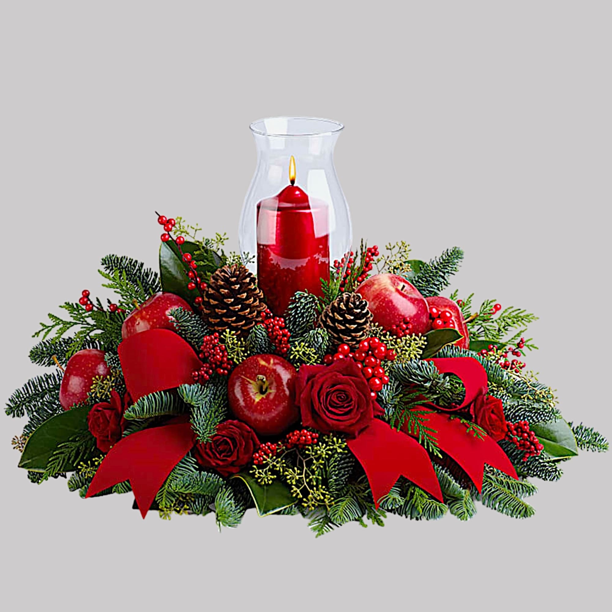 Holiday centerpiece with red roses, apples, pinecones, and a candle in a glass hurricane