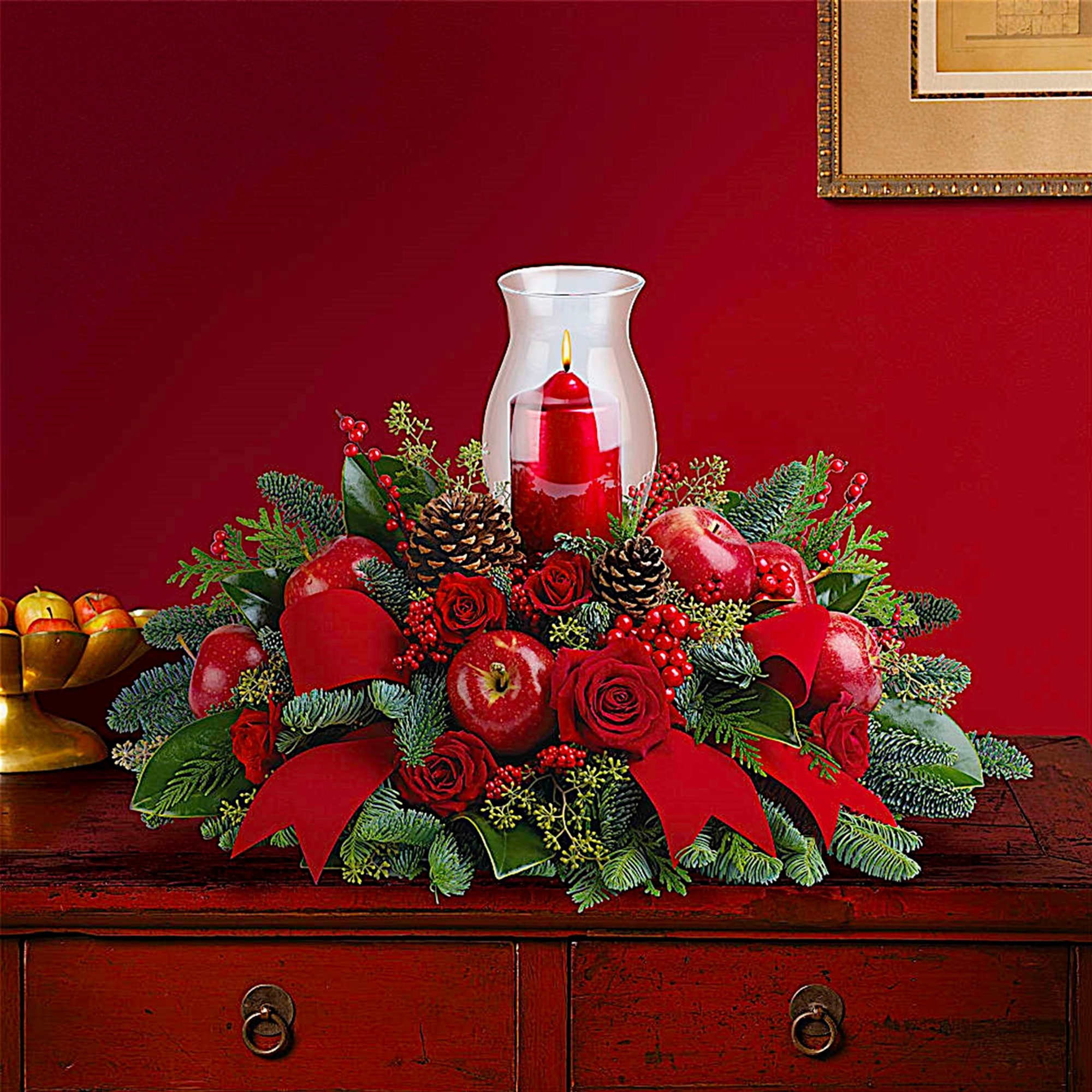 Red floral centerpiece with apples and a candle in a glass hurricane vase