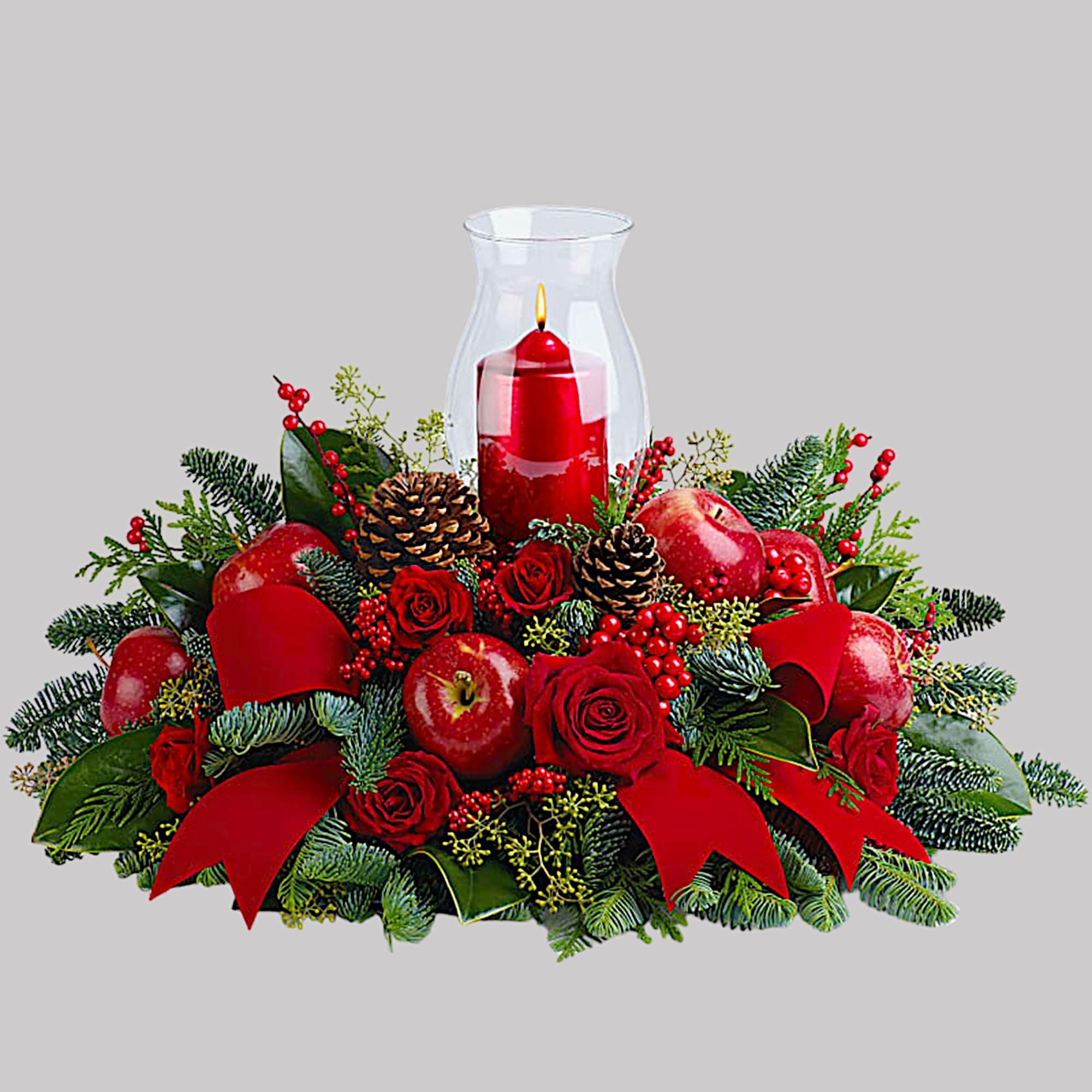 Red candle centerpiece with apples, pinecones, and roses in a glass hurricane