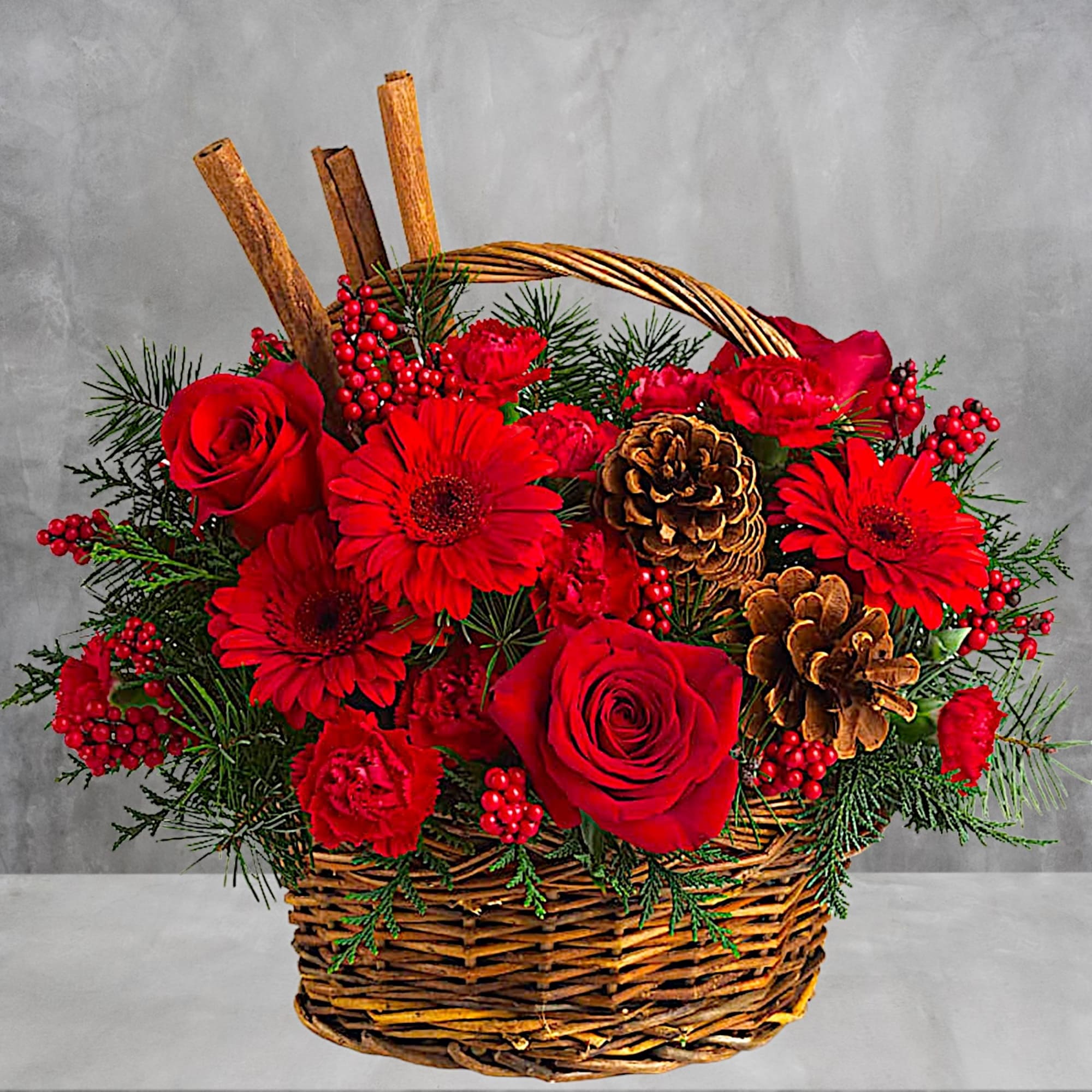 Red roses and gerbera daisies in a wicker basket with pinecones and berries