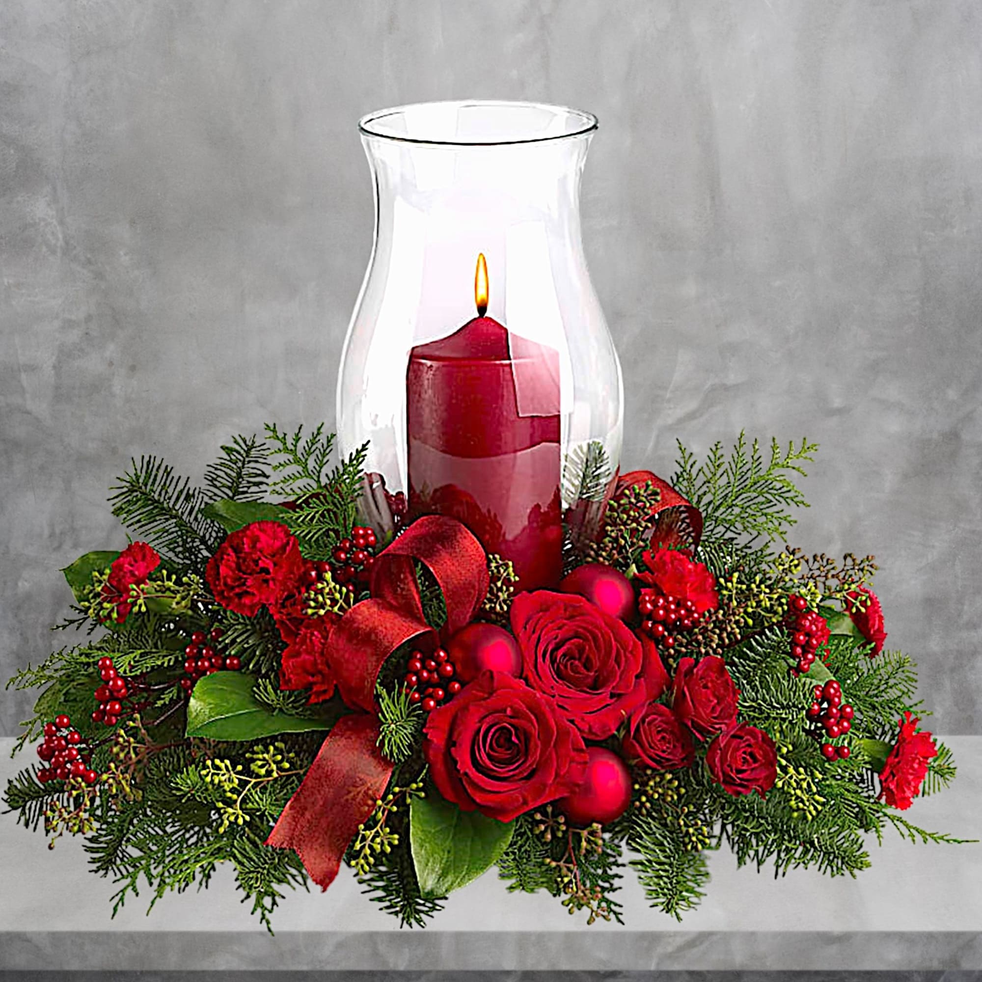 Red candle in a glass hurricane surrounded by red roses and greenery