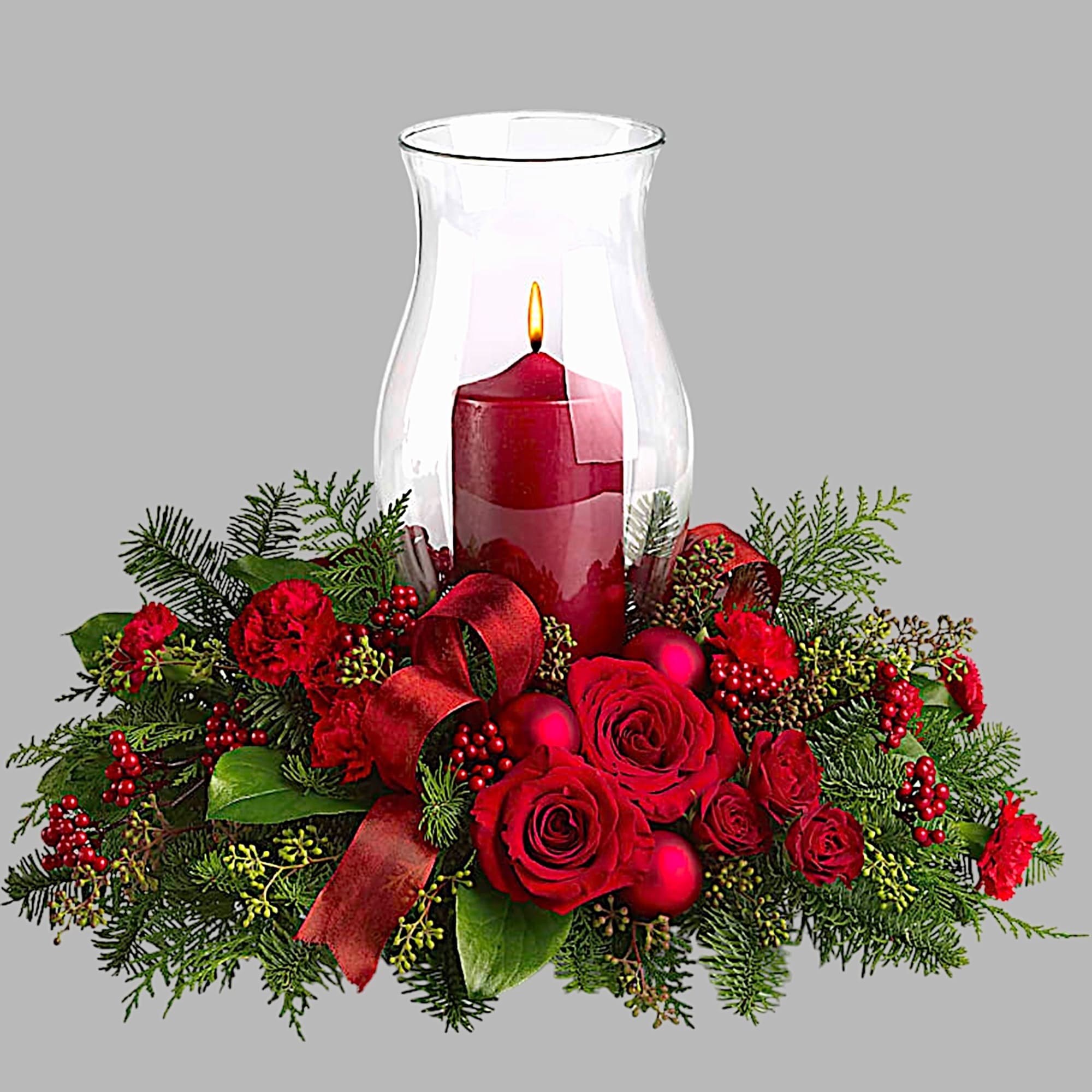 Red roses and carnations arranged around a red candle in a glass hurricane vase