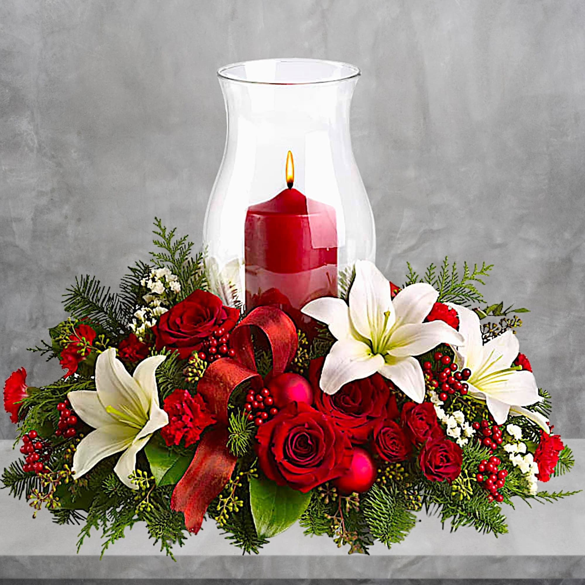 Red roses and white lilies arranged around a red candle in a glass hurricane vase