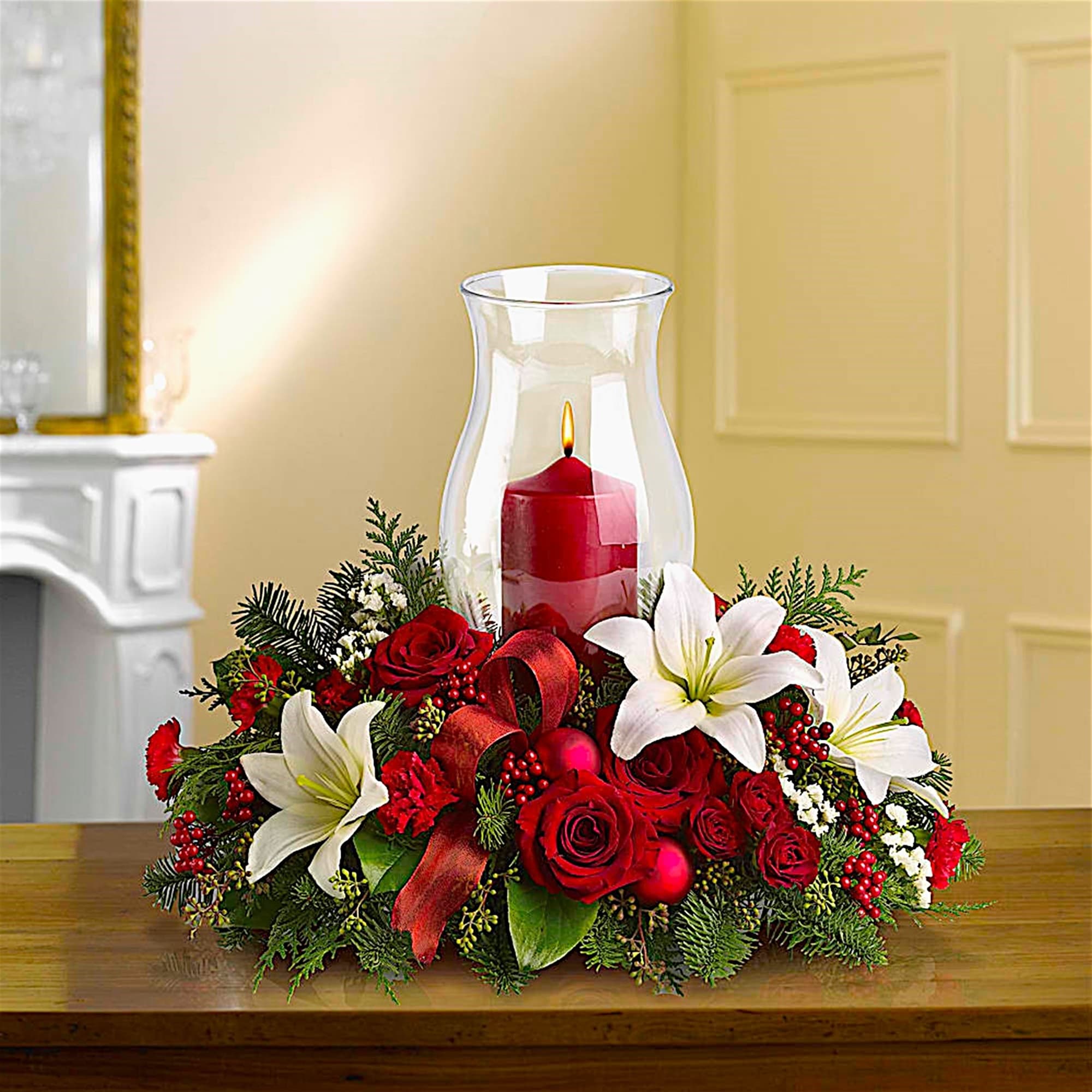 Red roses and white lilies arranged around a glass hurricane candle holder