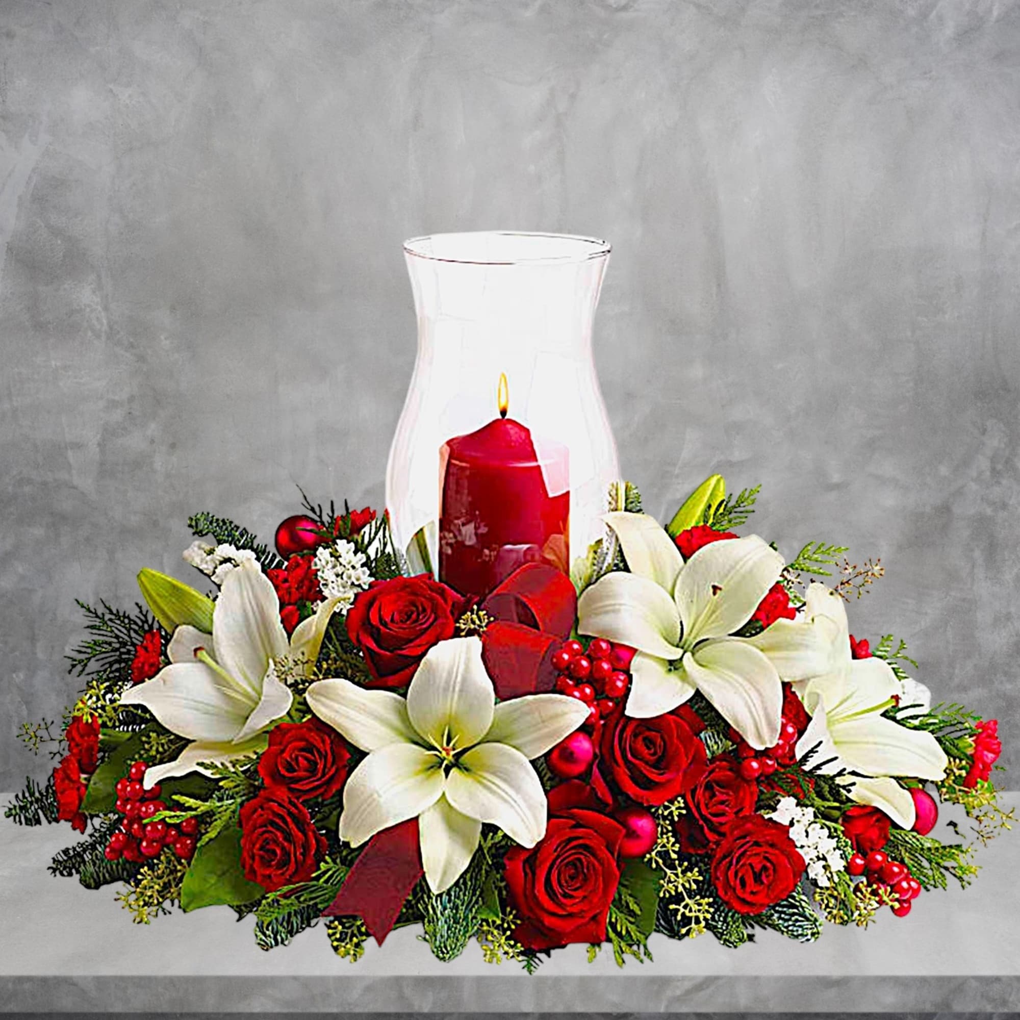 Red roses and white lilies arranged around a red candle in a glass hurricane vase