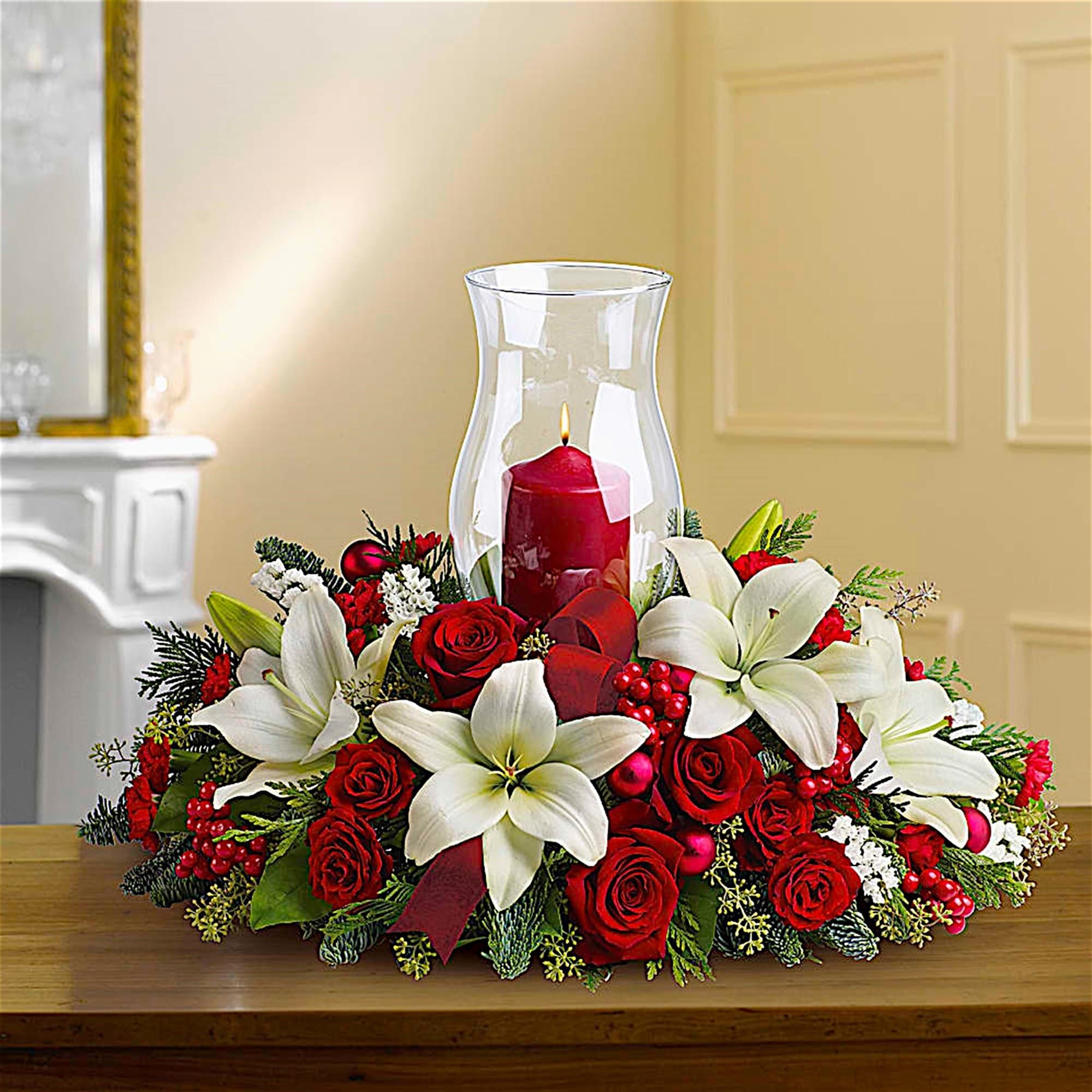 Red roses and white lilies arranged around a red candle in a glass hurricane