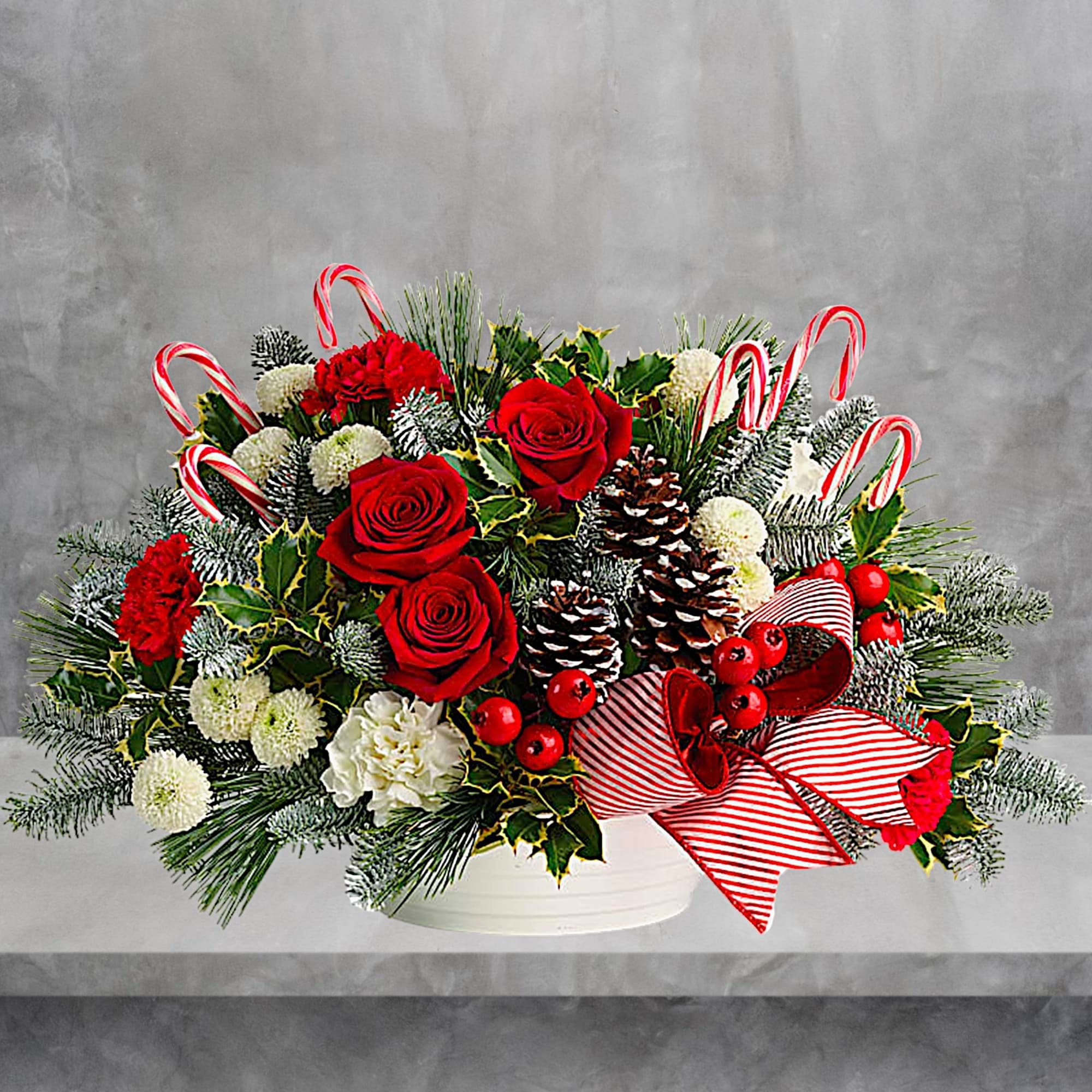 Holiday floral arrangement with red roses, white blooms, and candy canes in a white vase