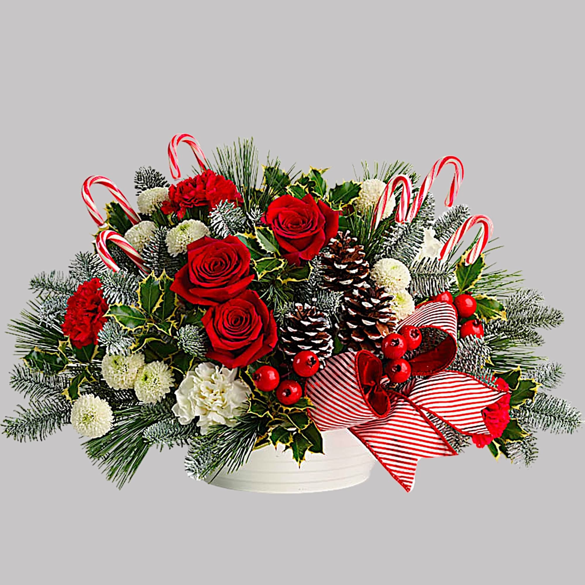 Holiday floral arrangement with red roses, carnations, and candy canes in a white bowl