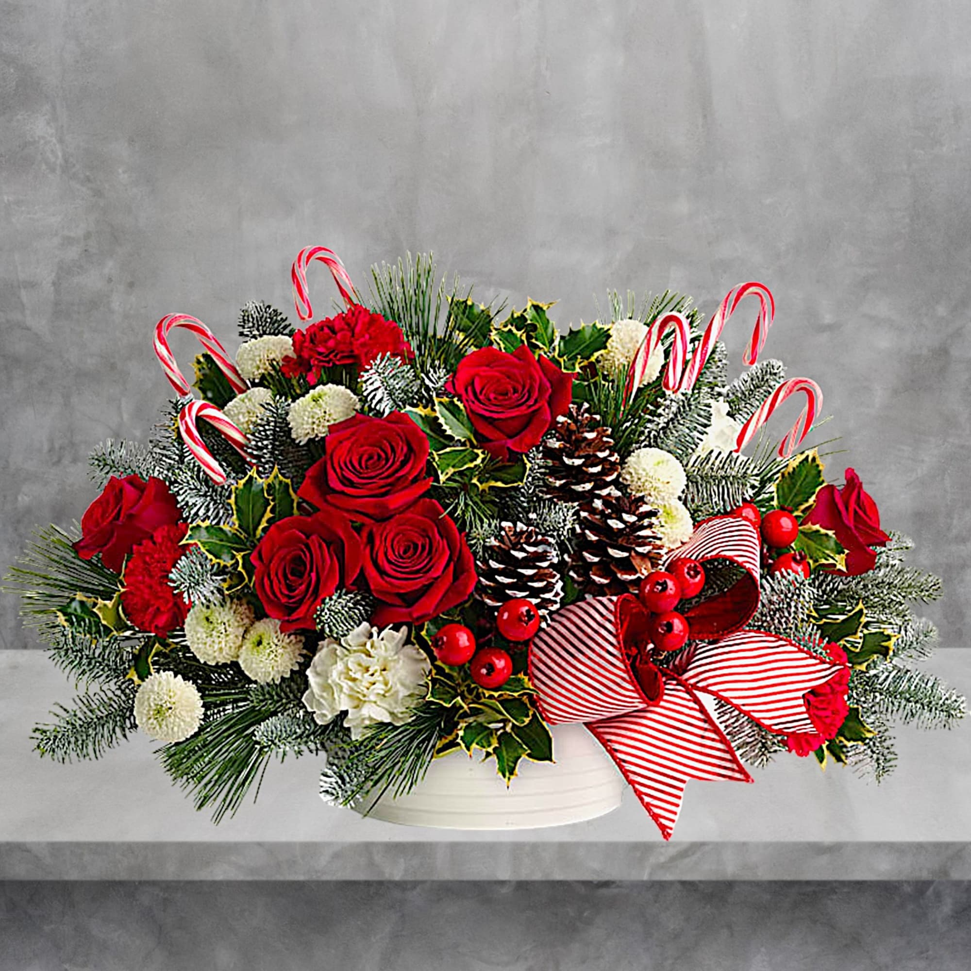 Christmas bouquet with red roses, white blooms, candy canes, and pinecones in a white container