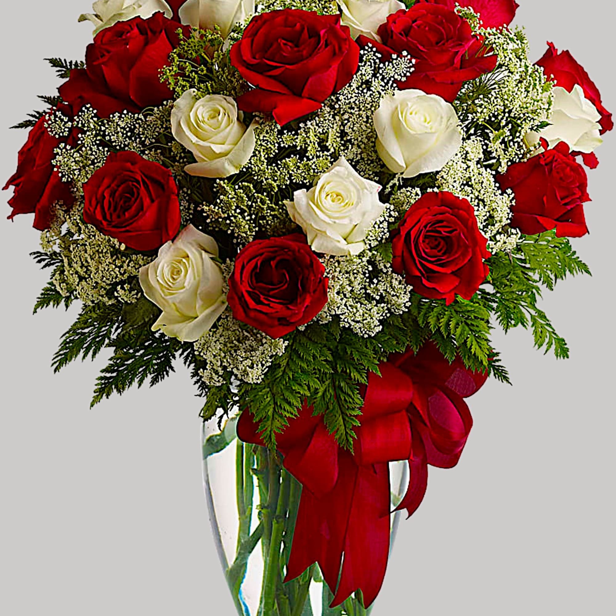 Red and white roses in a clear glass vase with a red ribbon