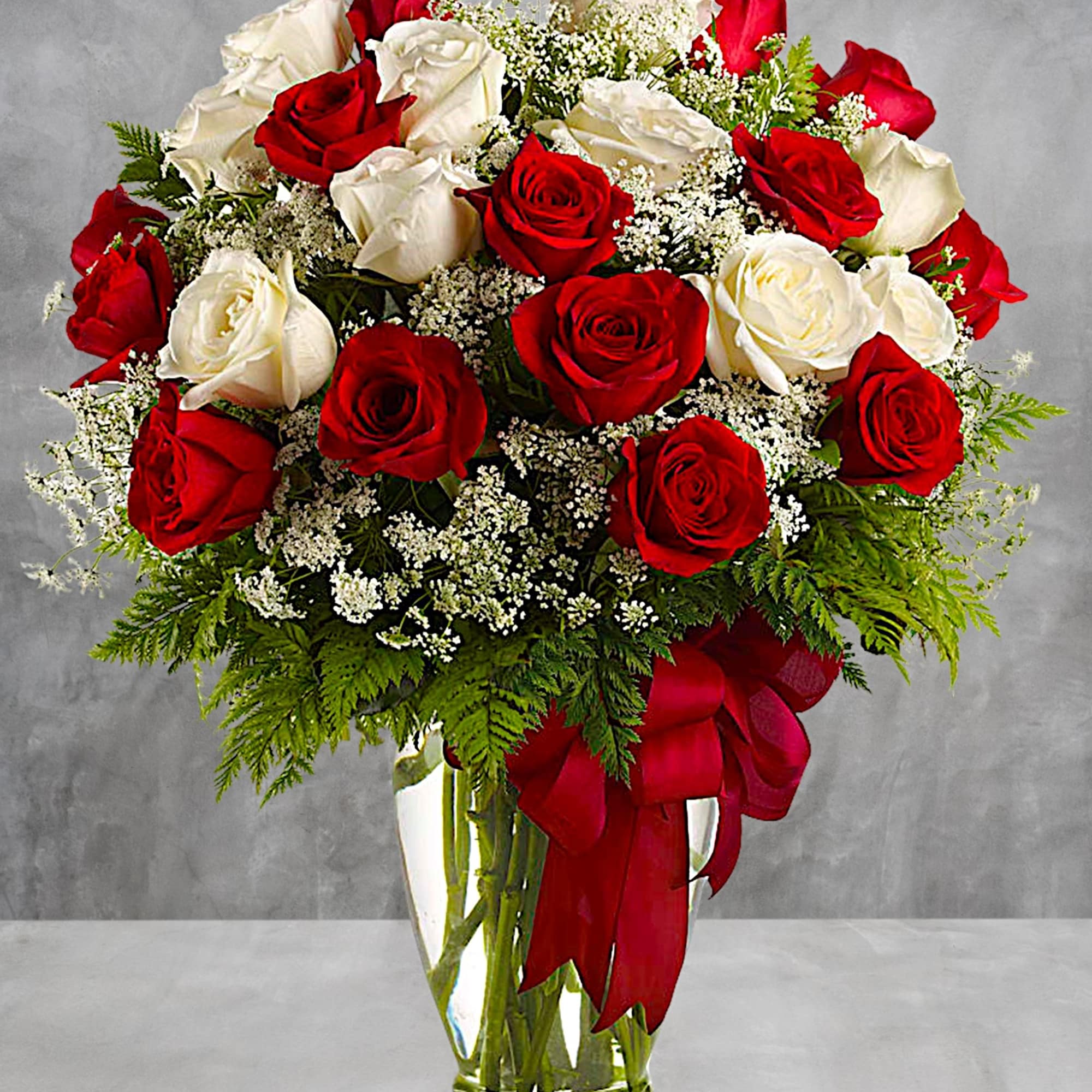 Red and white roses arranged in a clear glass vase with a red ribbon