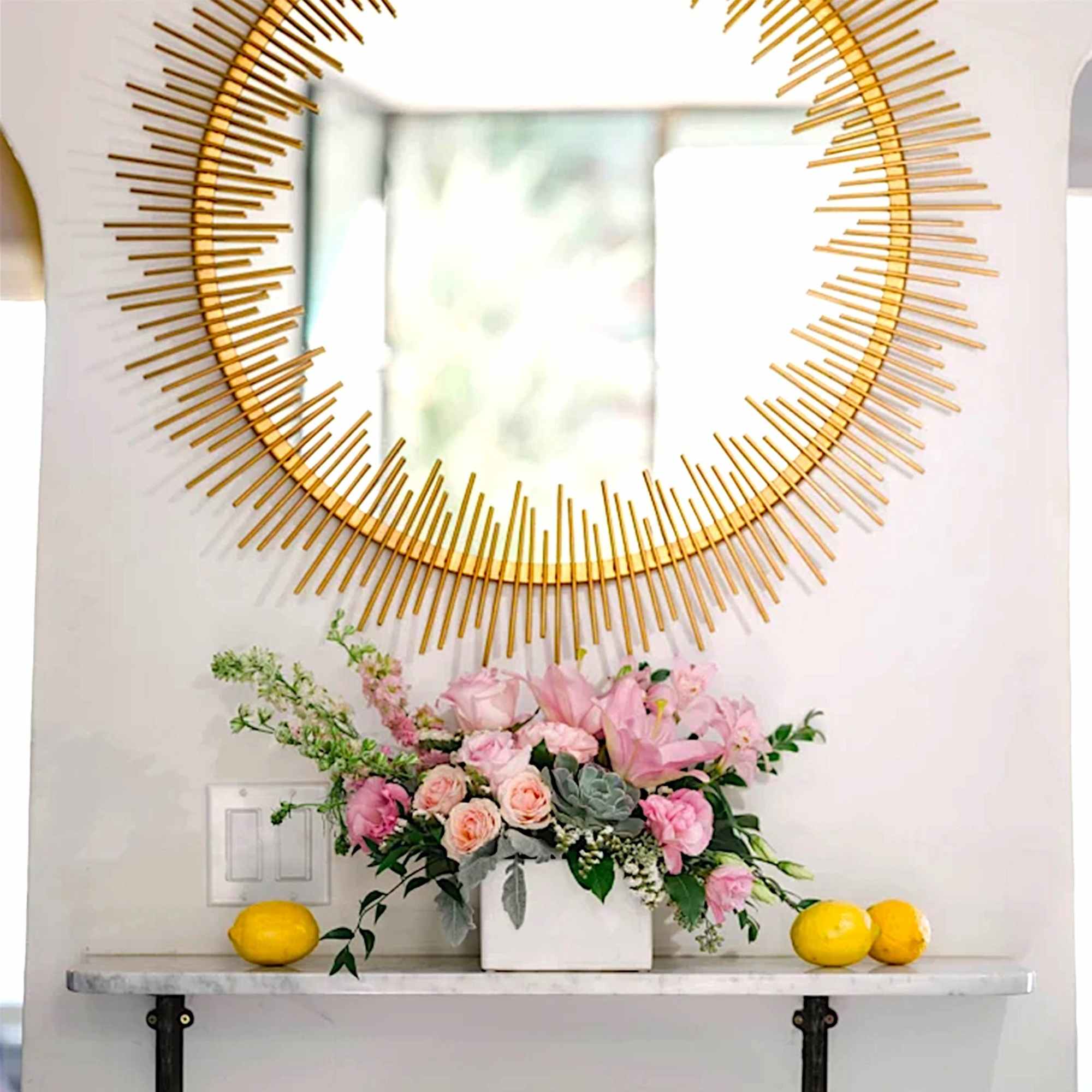 Pink floral arrangement in a white rectangular vase beneath a gold sunburst mirror