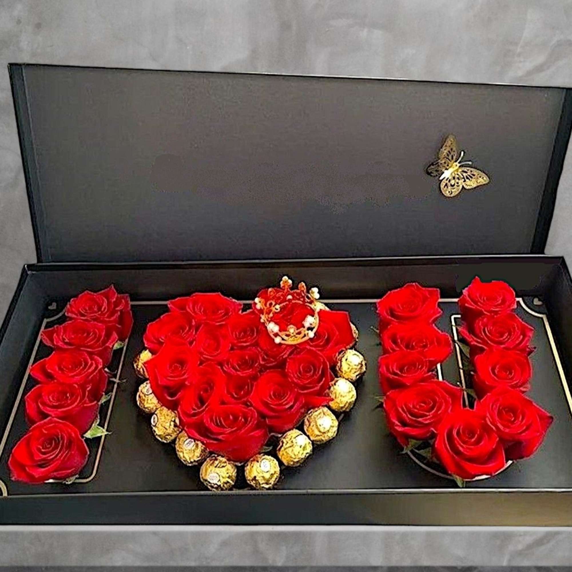 Red roses arranged in a gift box with chocolates and a butterfly decoration