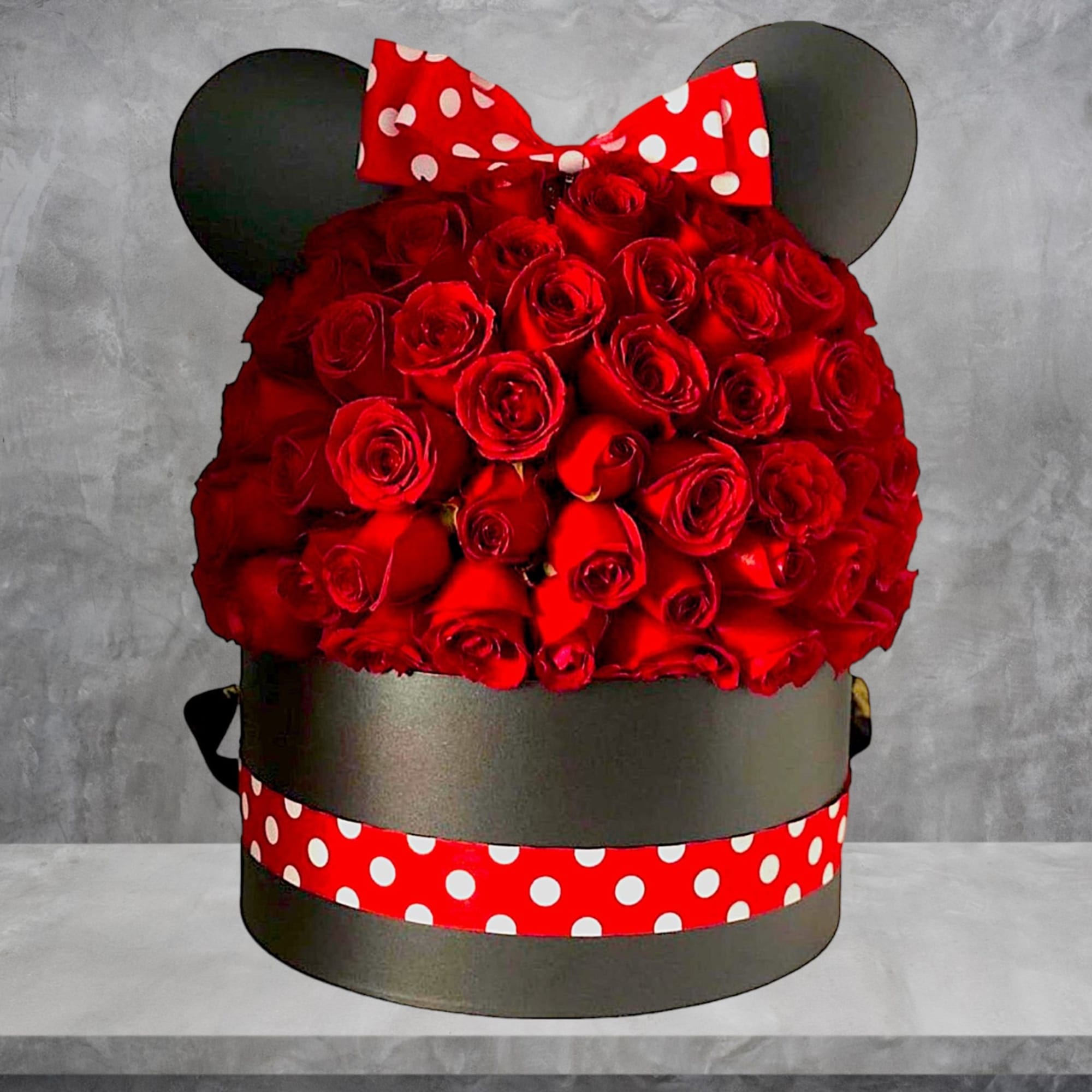 Red rose arrangement in a round black box with a polka-dot bow and ears