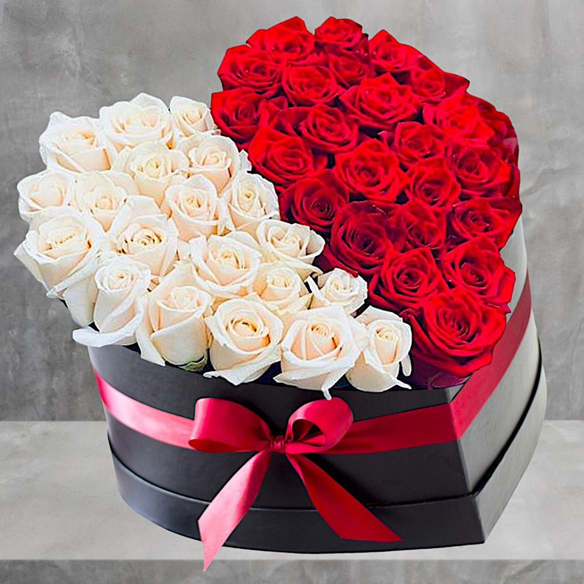 Heart-shaped box filled with red and white roses and tied with a pink ribbon