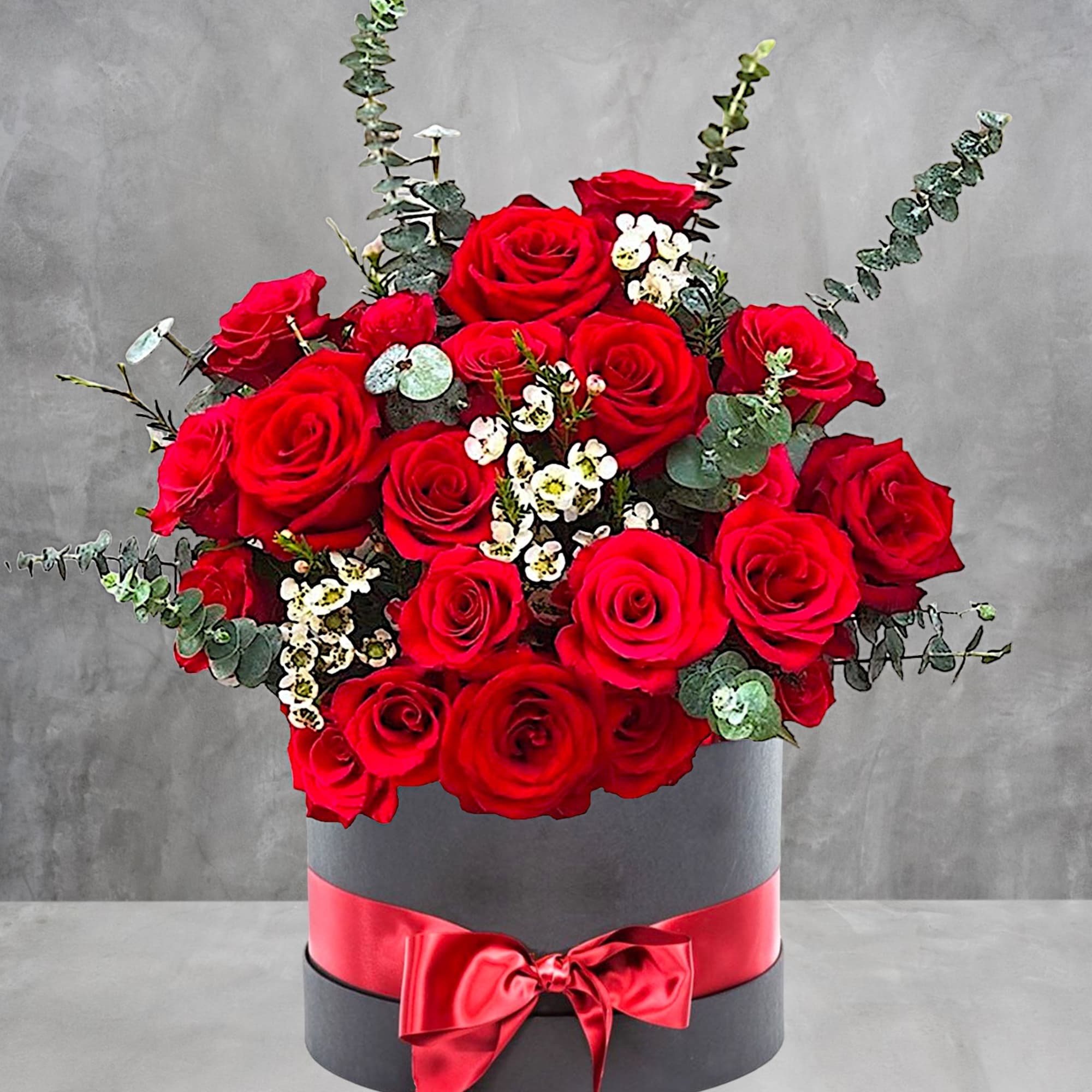 Red roses arranged in a round black box with a red ribbon