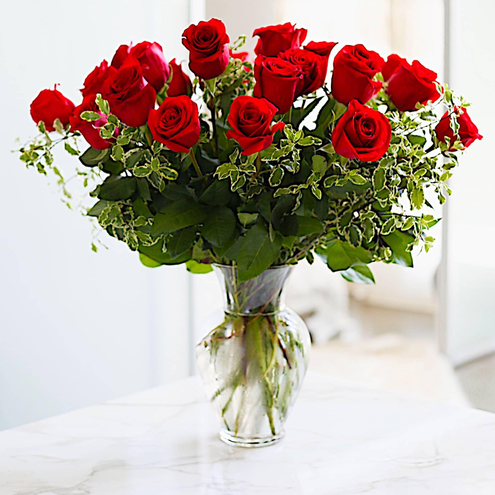 Red roses arranged in a clear glass vase with variegated greenery