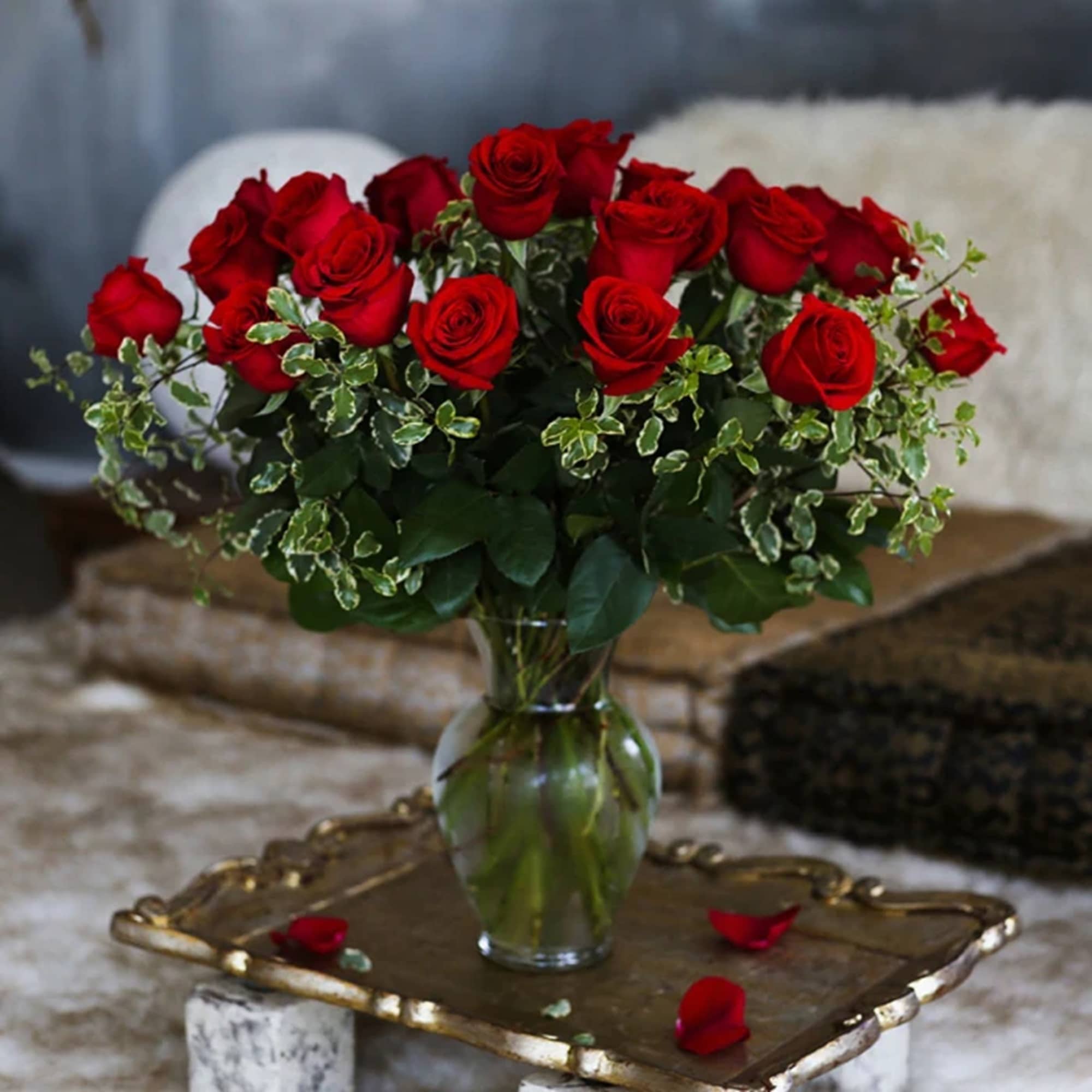 Red roses arranged in a clear glass vase with variegated greenery