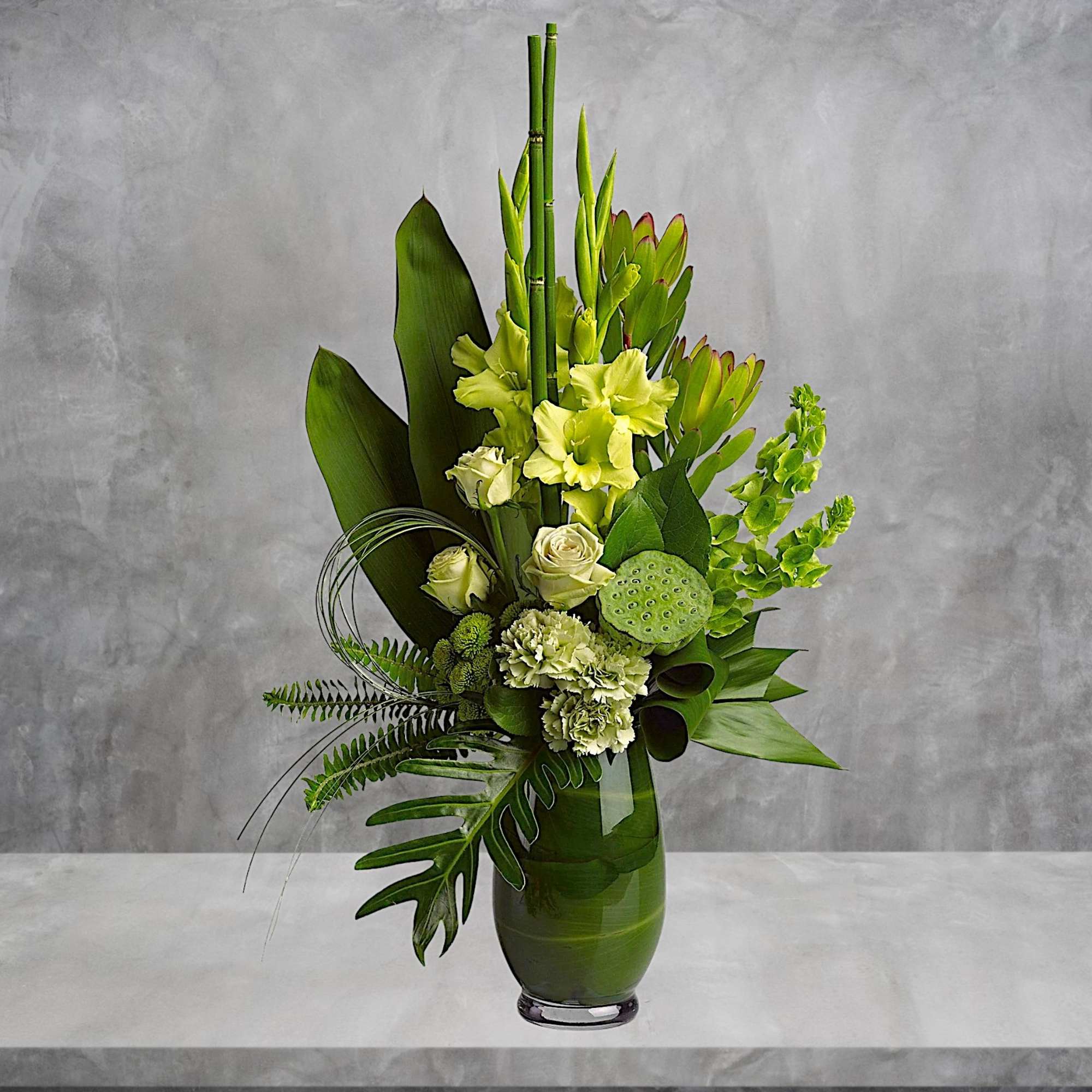 Tall green floral arrangement in a glass vase with pale yellow blooms