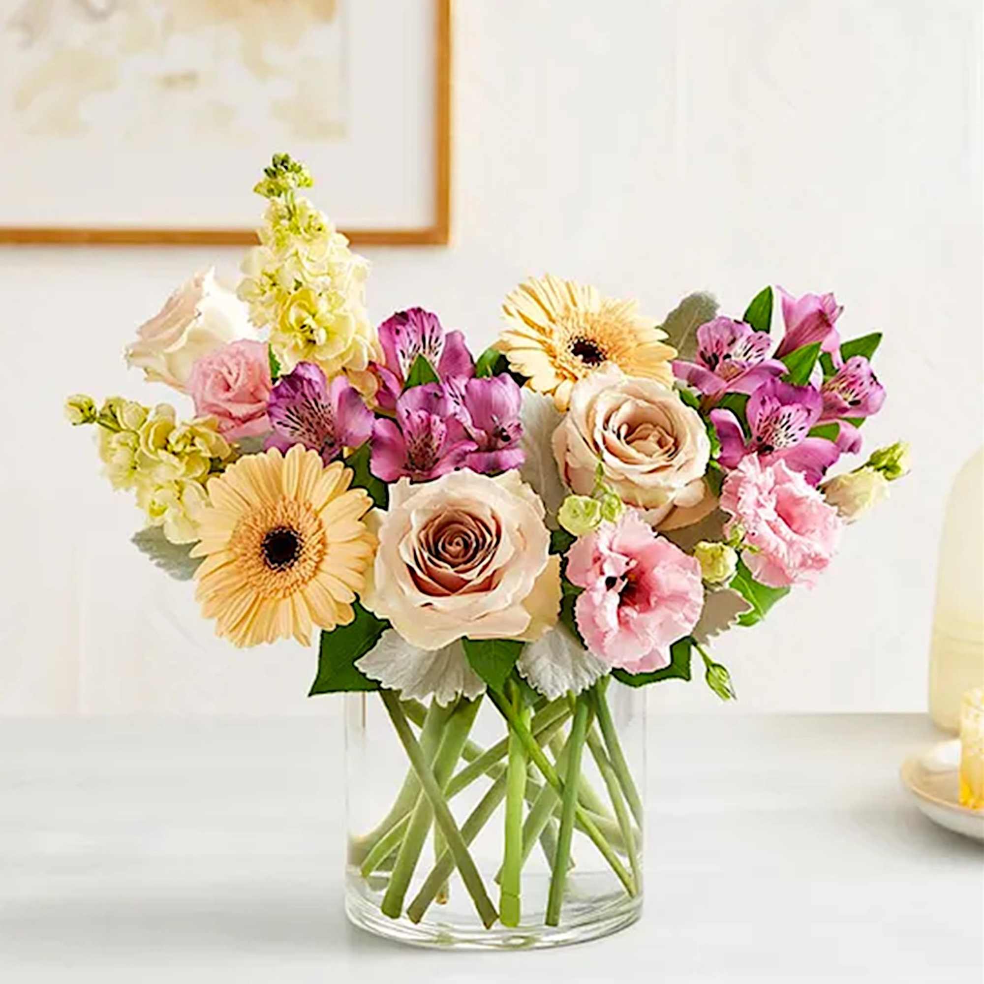 Mixed bouquet of roses, gerbera daisies, and pink blooms in a clear glass vase