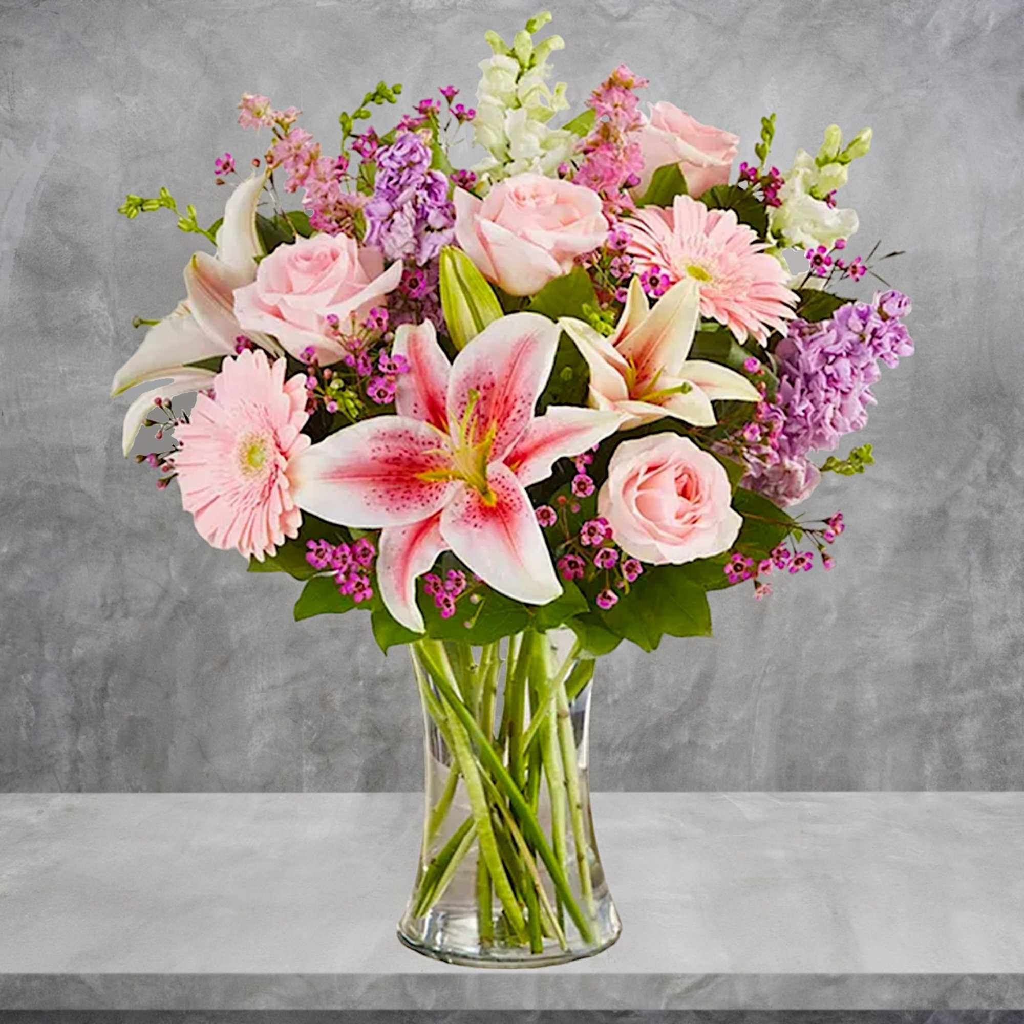 Bouquet of pink roses, lilies, and gerbera daisies in a clear glass vase
