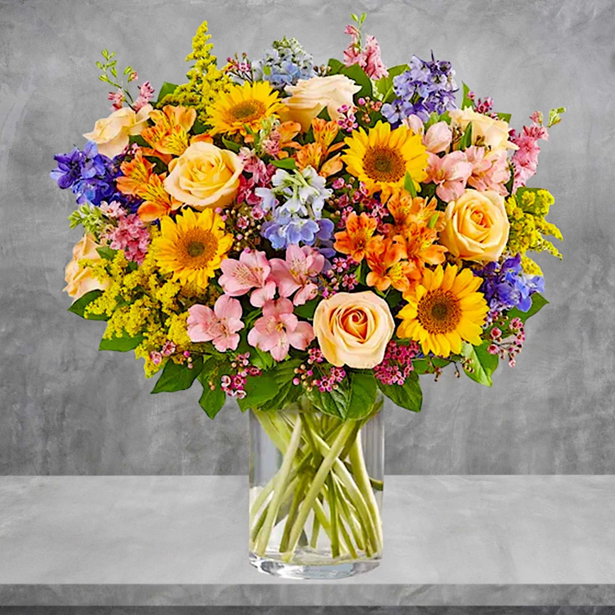 Mixed bouquet of roses, sunflowers, and pastel flowers in a glass vase