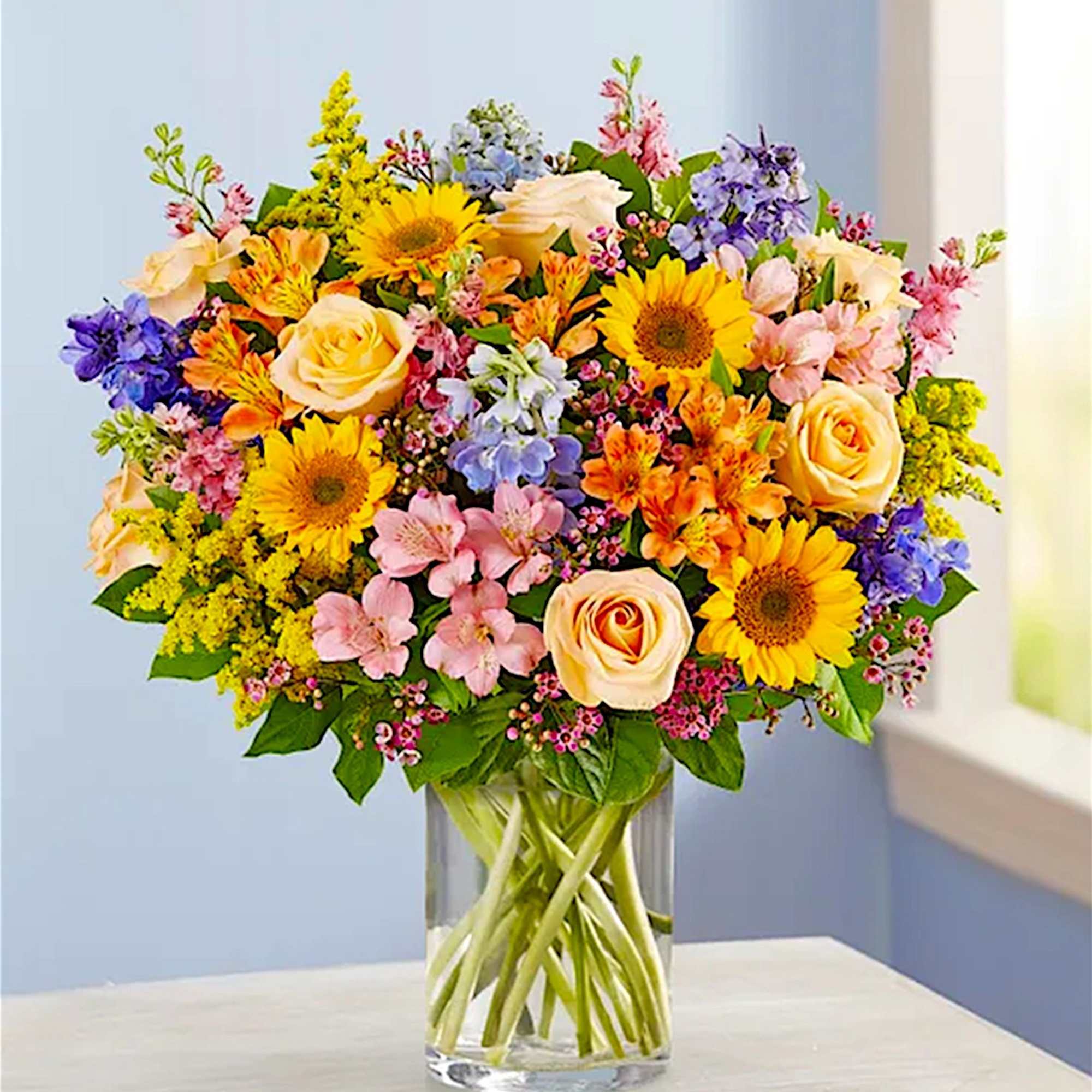 Mixed bouquet of sunflowers, roses, and pastel flowers in a clear glass vase, photo 2 of 6