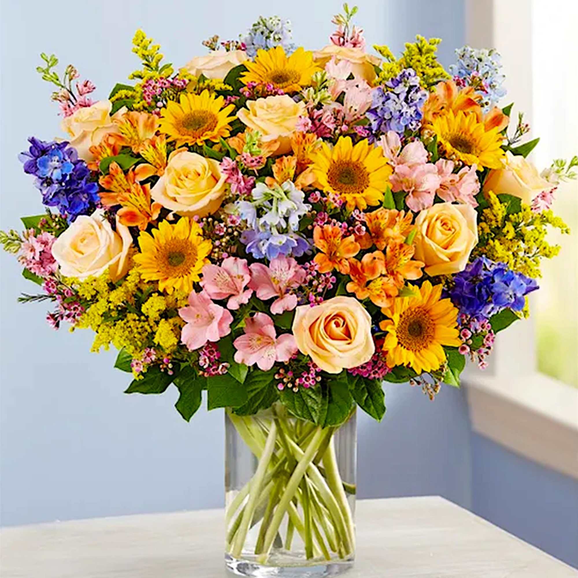 Mixed bouquet of roses, sunflowers, and colorful blooms in a glass vase