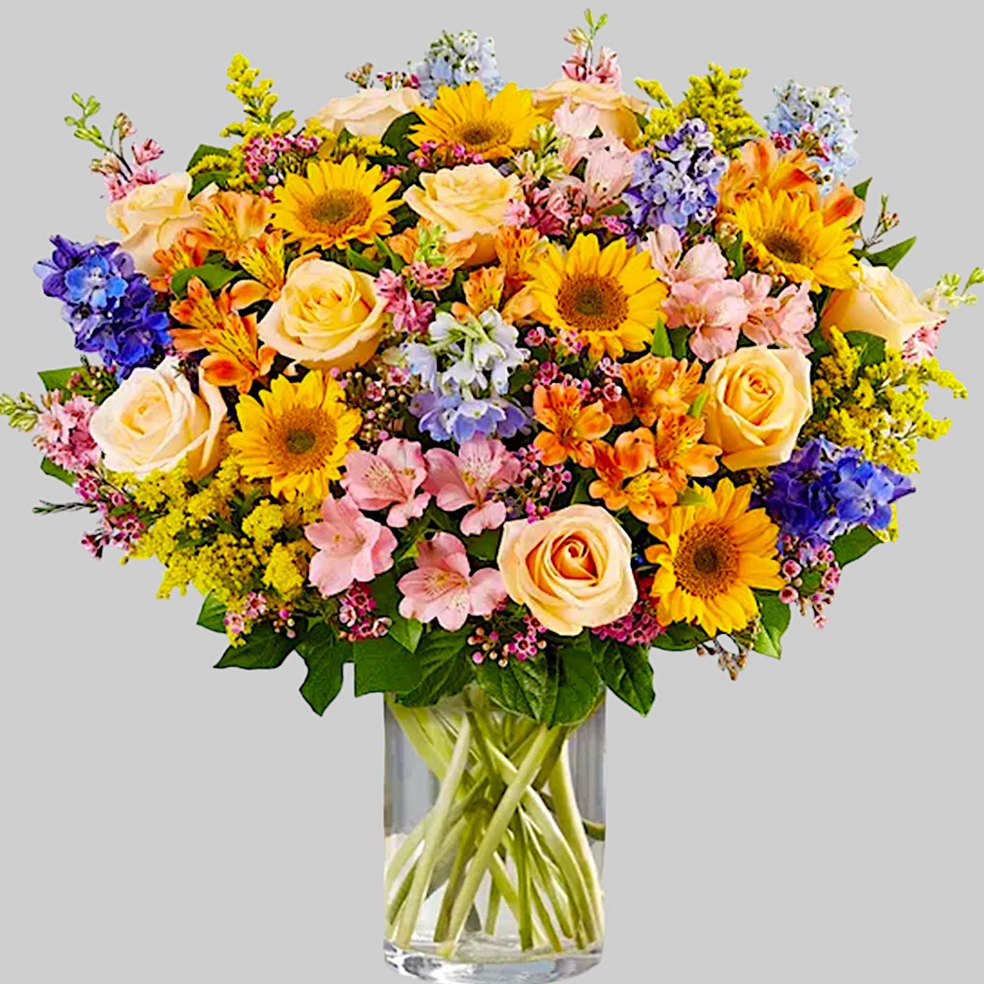 Mixed bouquet of yellow sunflowers, peach roses, and pastel flowers in a glass vase
