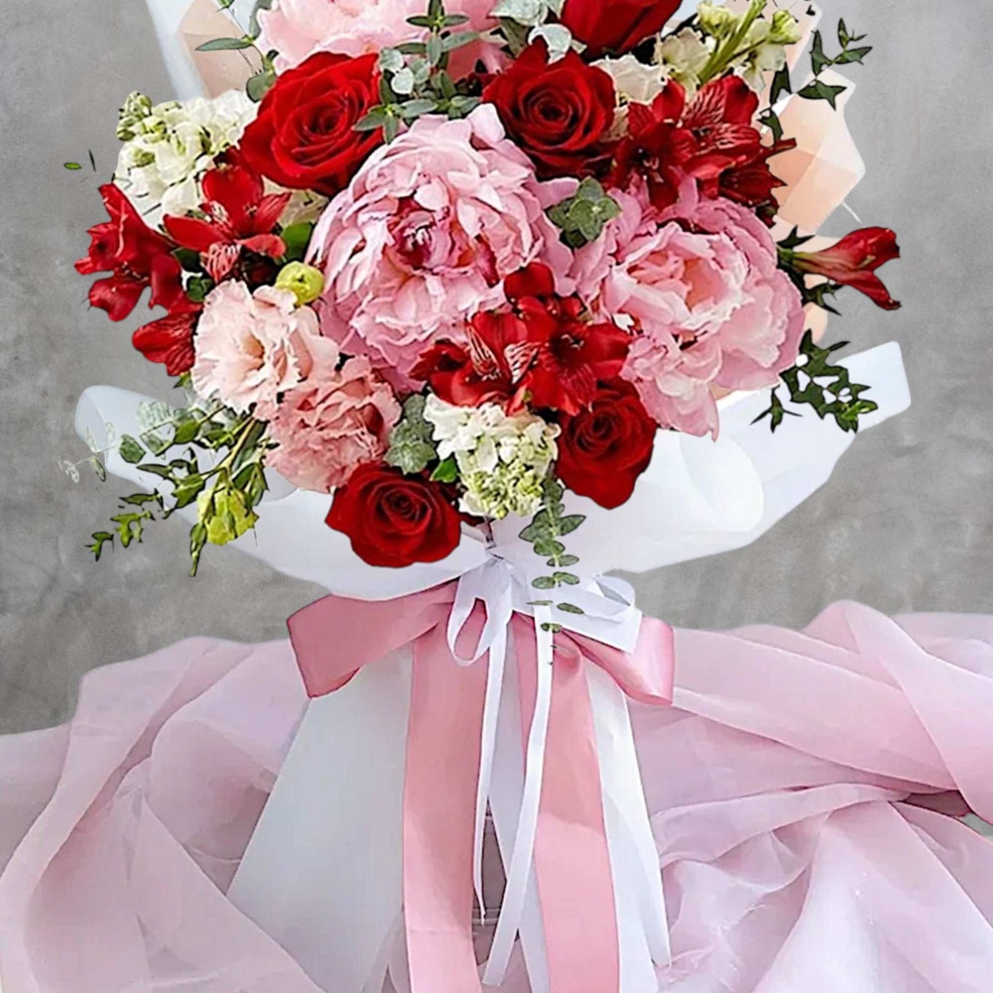 Bouquet of pink and red flowers wrapped in white paper with ribbon