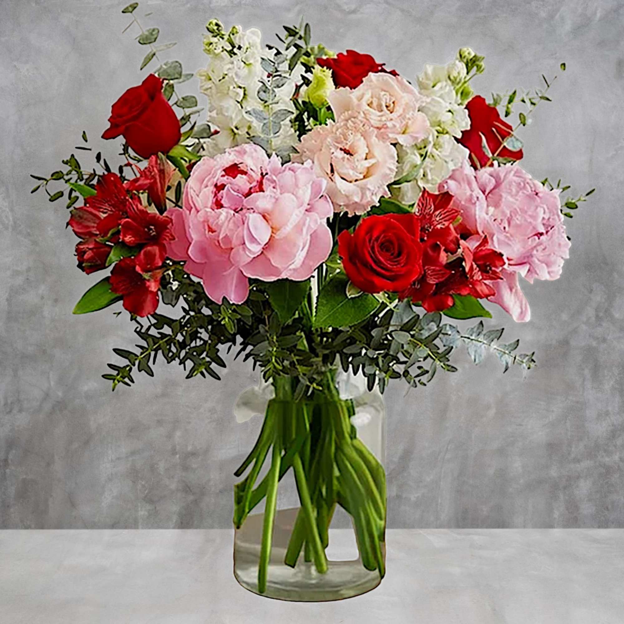 Bouquet of red roses, pink hydrangeas, and white blooms in a clear glass vase
