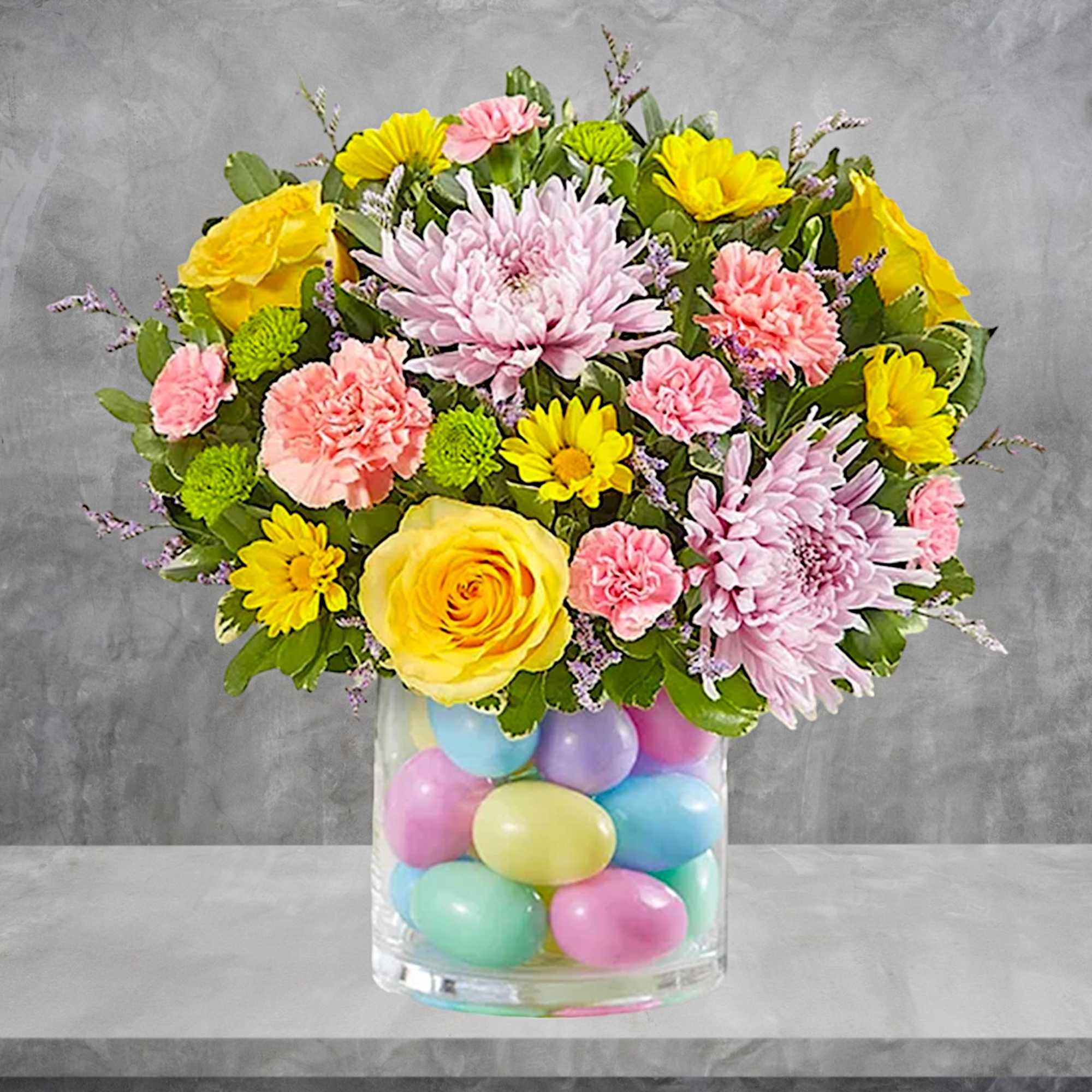 Bouquet of yellow, pink, and lavender flowers in a glass vase filled with pastel eggs