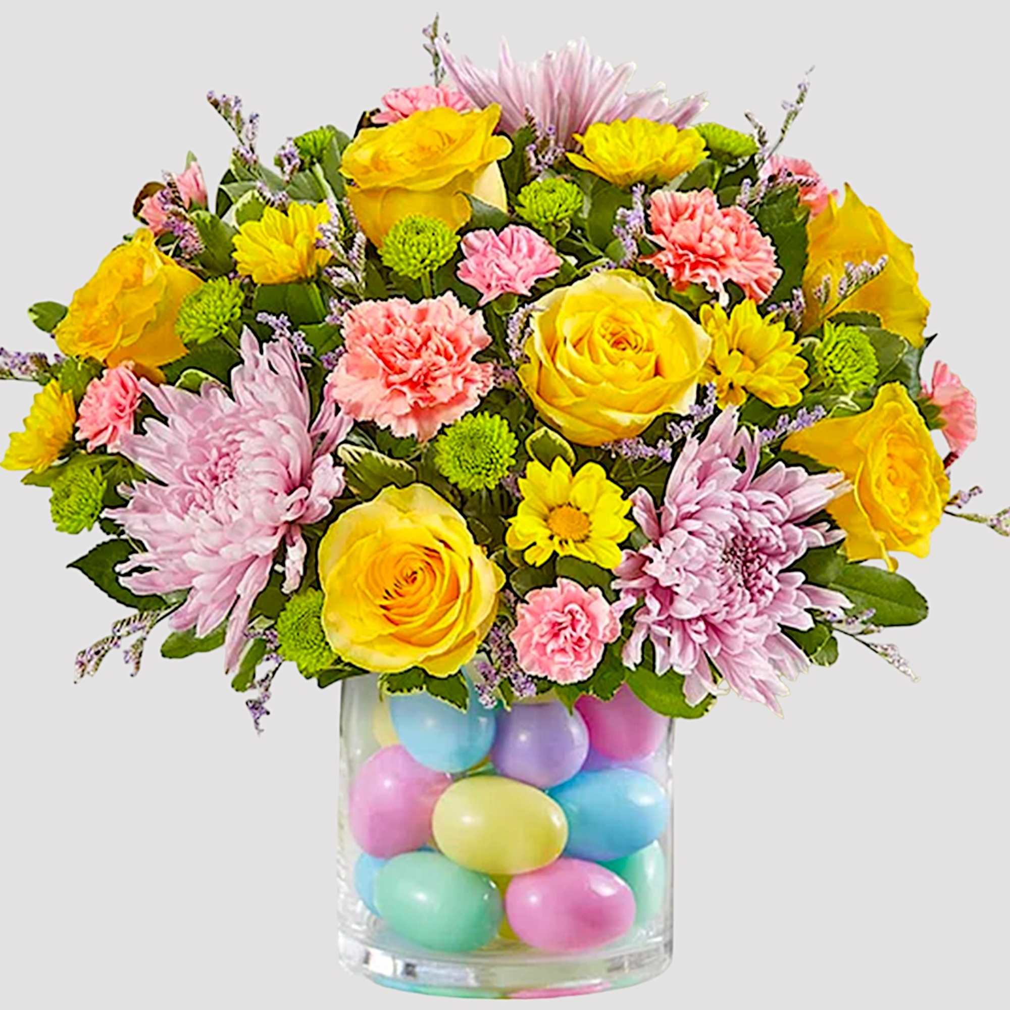Bouquet of yellow roses, pink chrysanthemums, and carnations in a glass vase with pastel eggs
