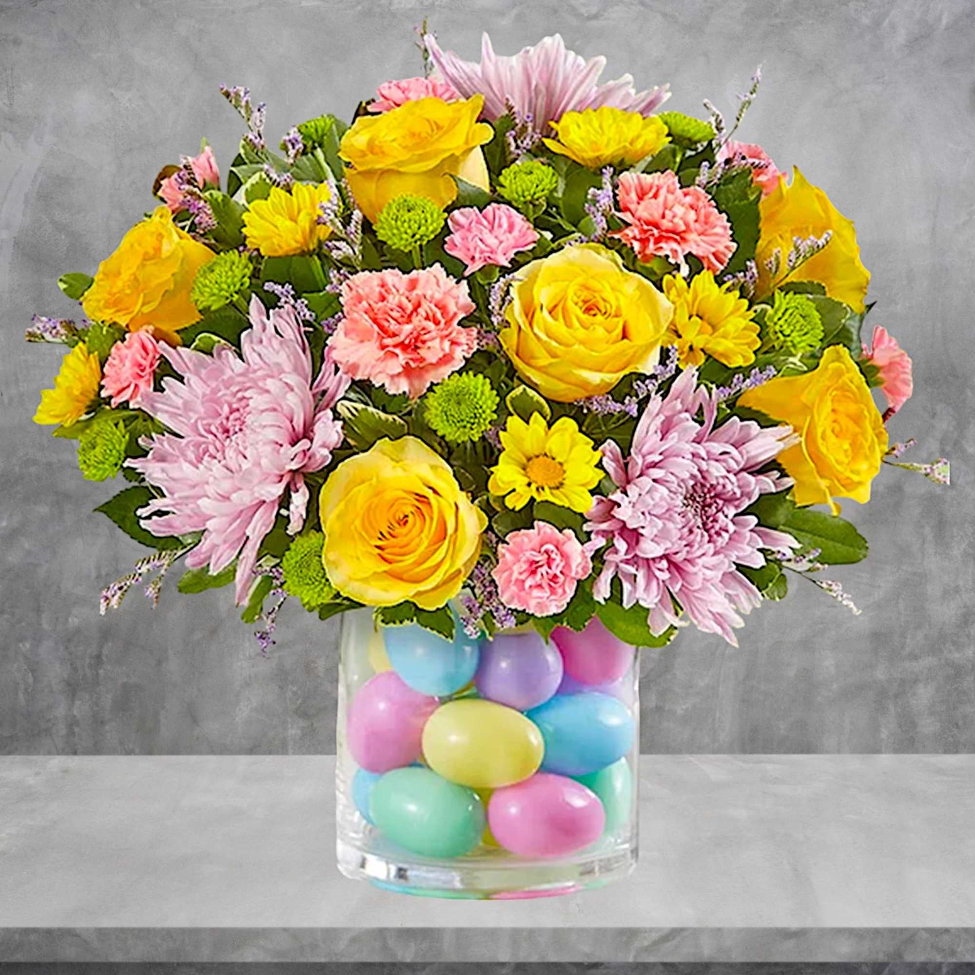 Bright mixed bouquet in a clear vase filled with pastel eggs