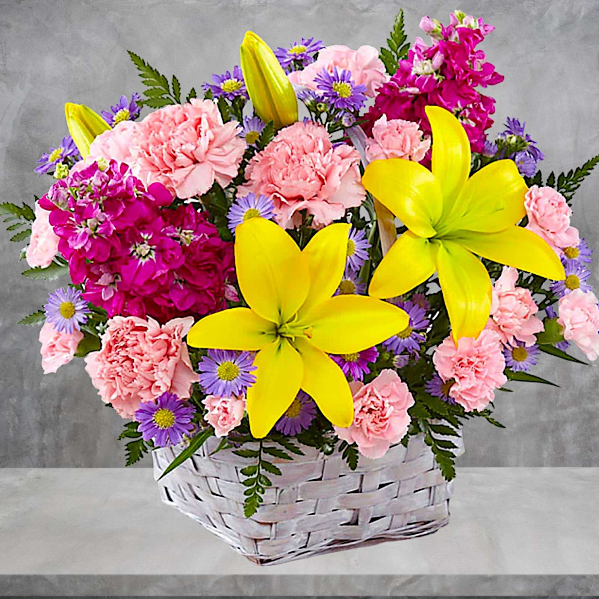 Basket arrangement of pink carnations, yellow lilies, and purple daisies