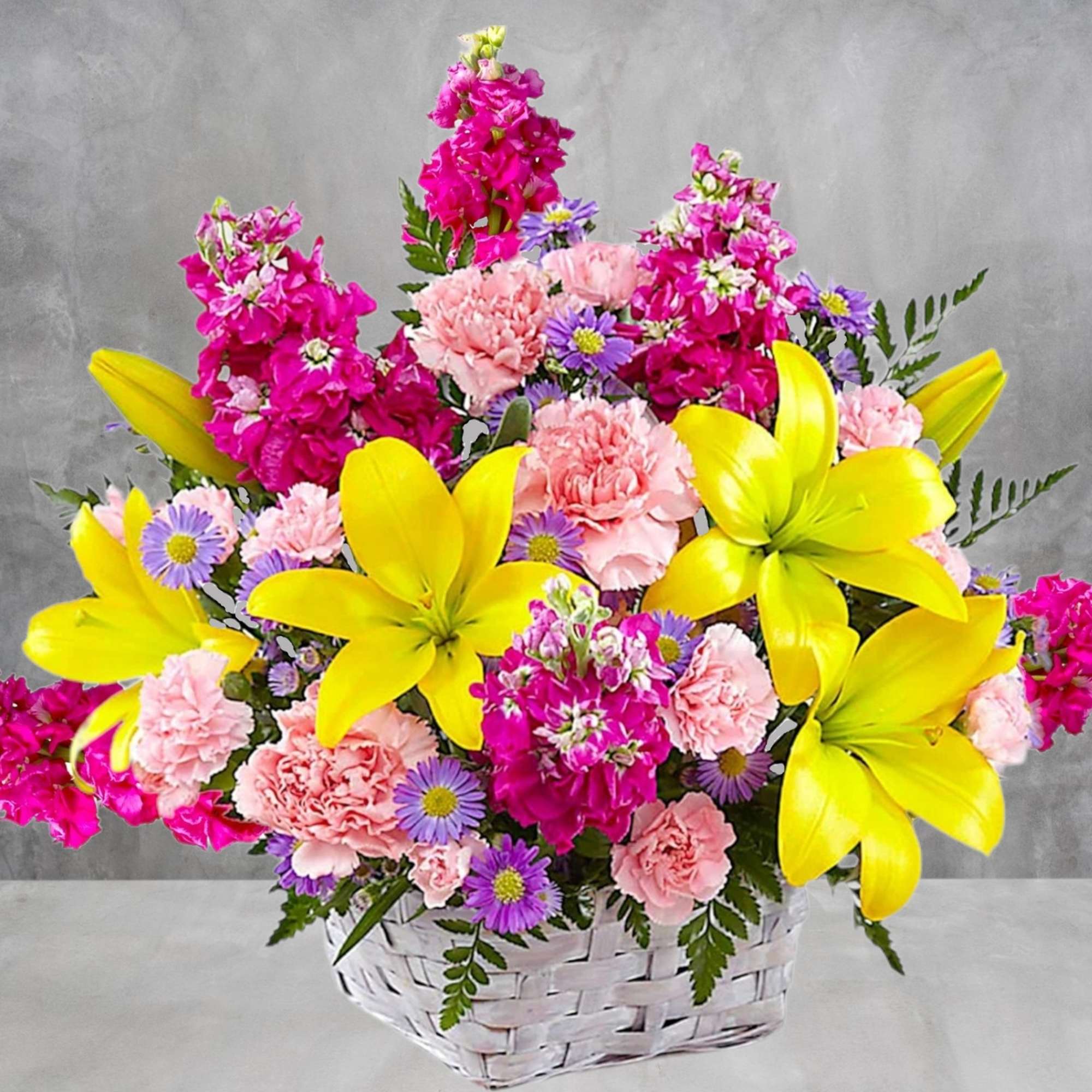 Basket arrangement of yellow lilies, pink carnations, and purple daisies