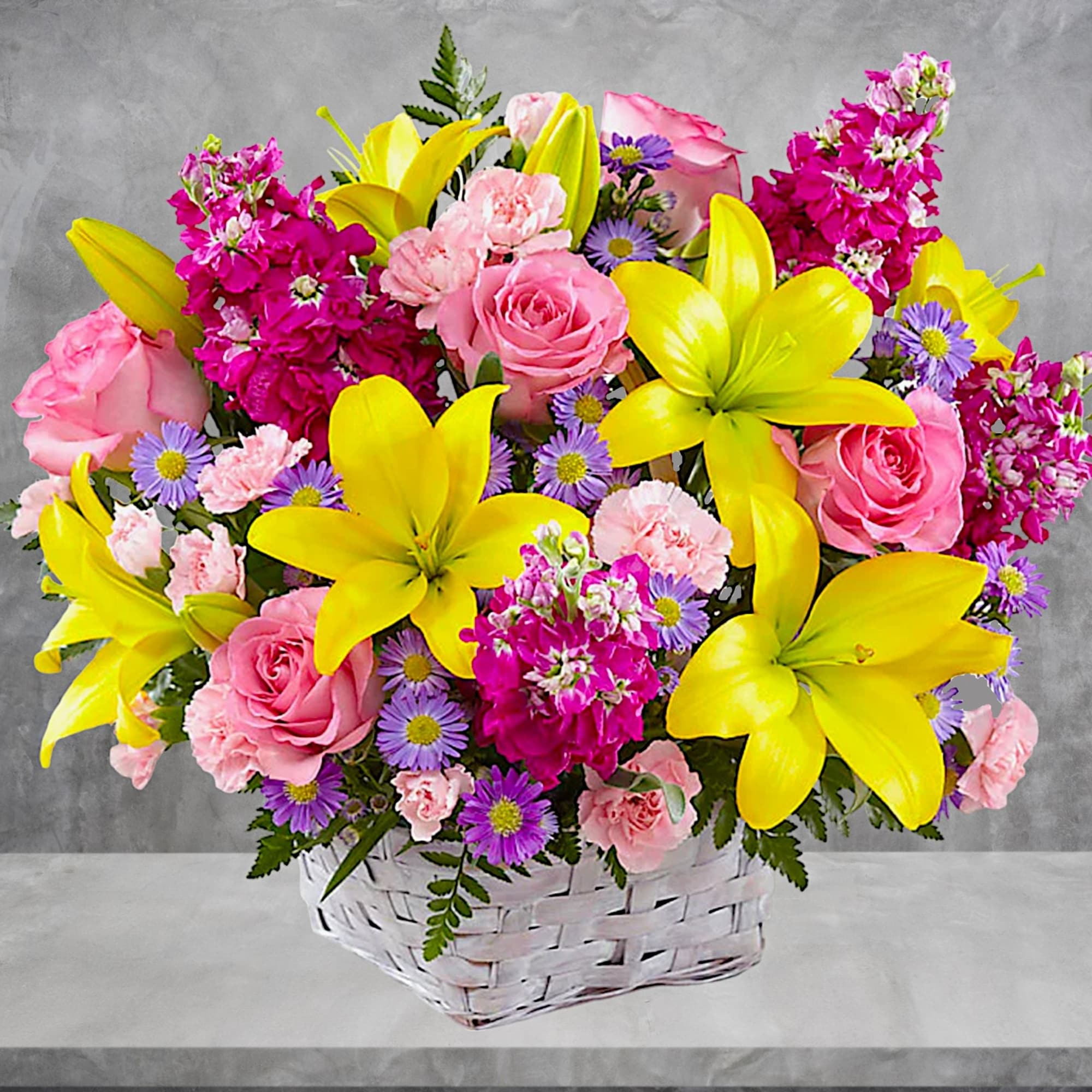 Basket arrangement of pink roses, yellow lilies, and purple daisies