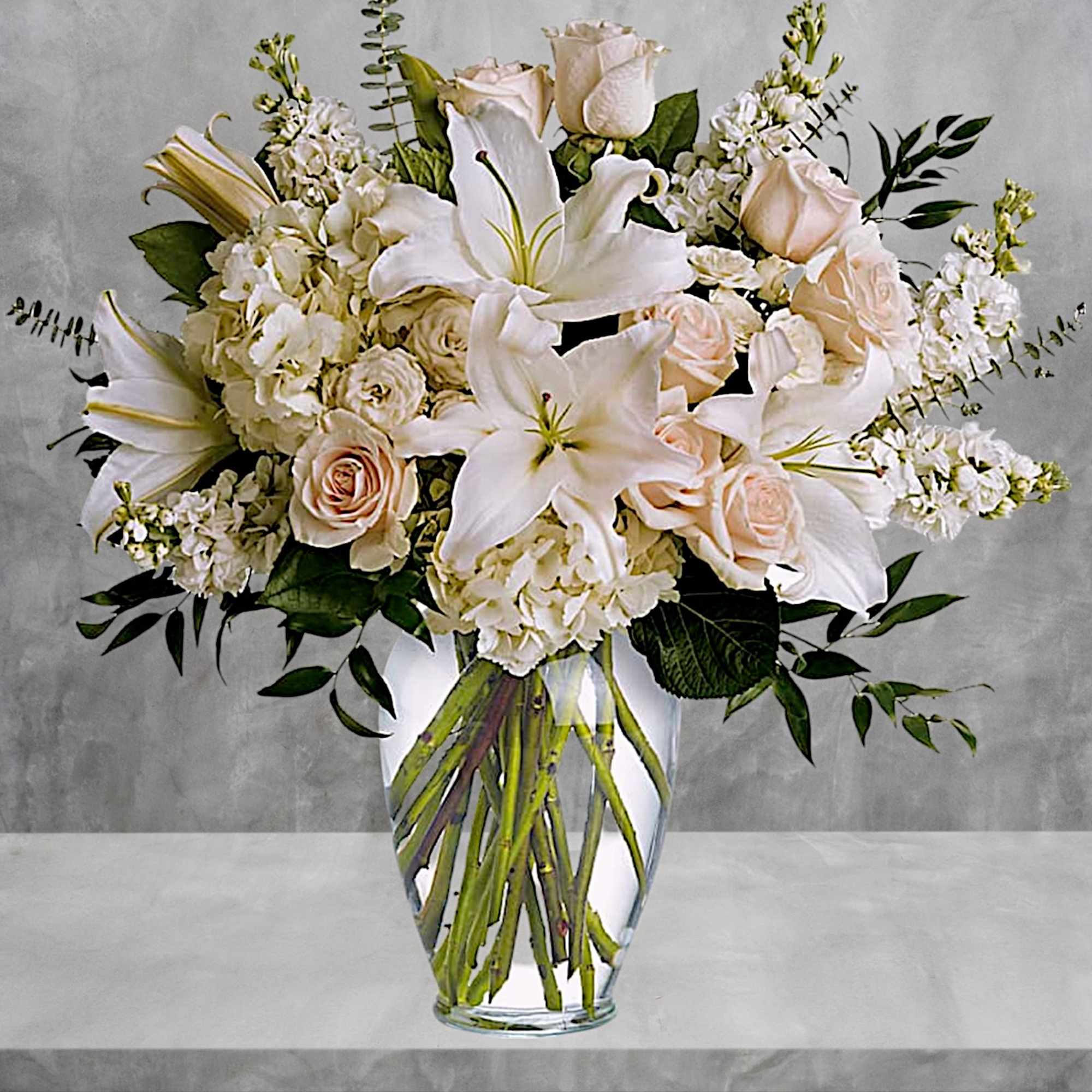 White lilies and pale roses arranged in a clear glass vase, photo 3 of 5