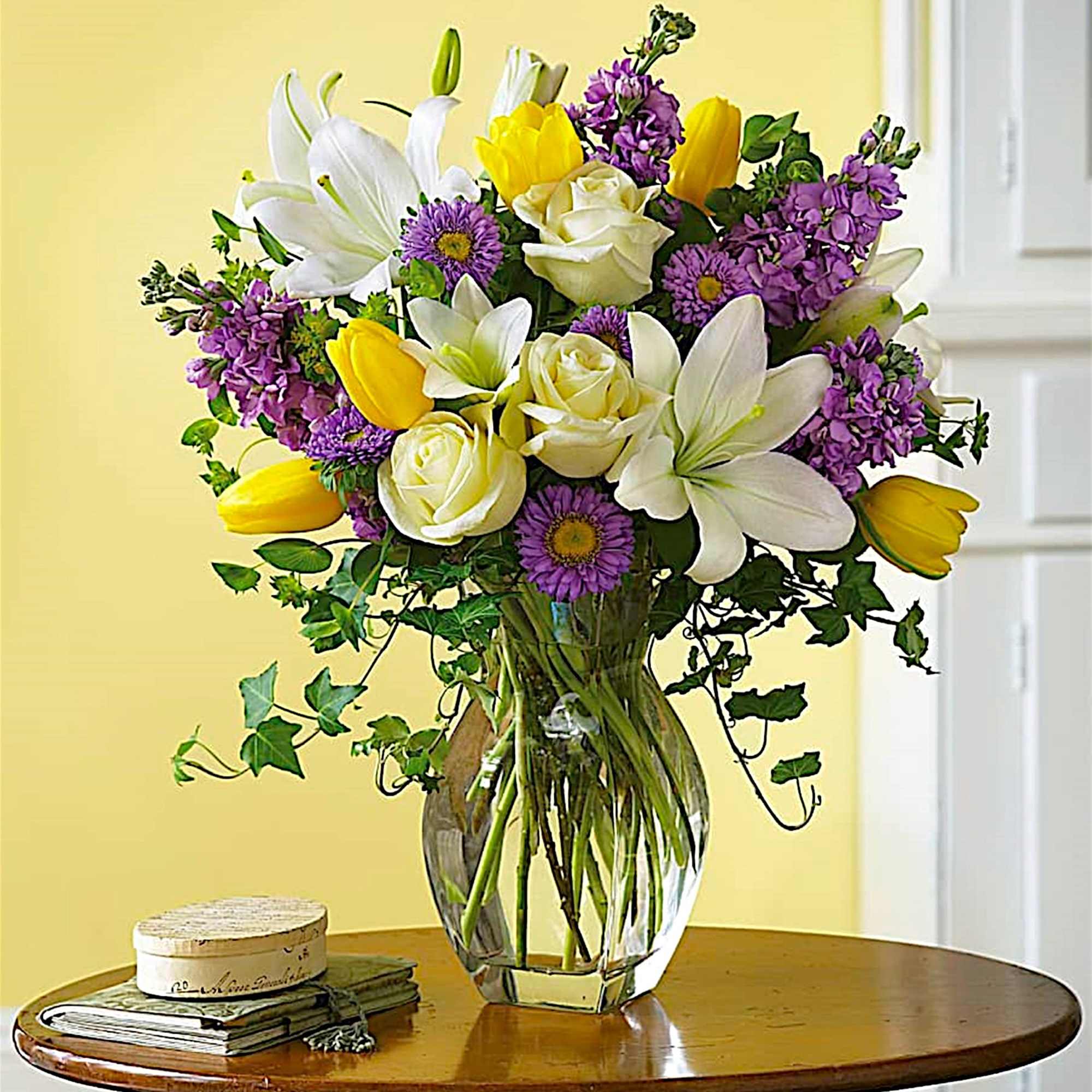 Bouquet of white lilies, yellow tulips, and purple flowers in a glass vase